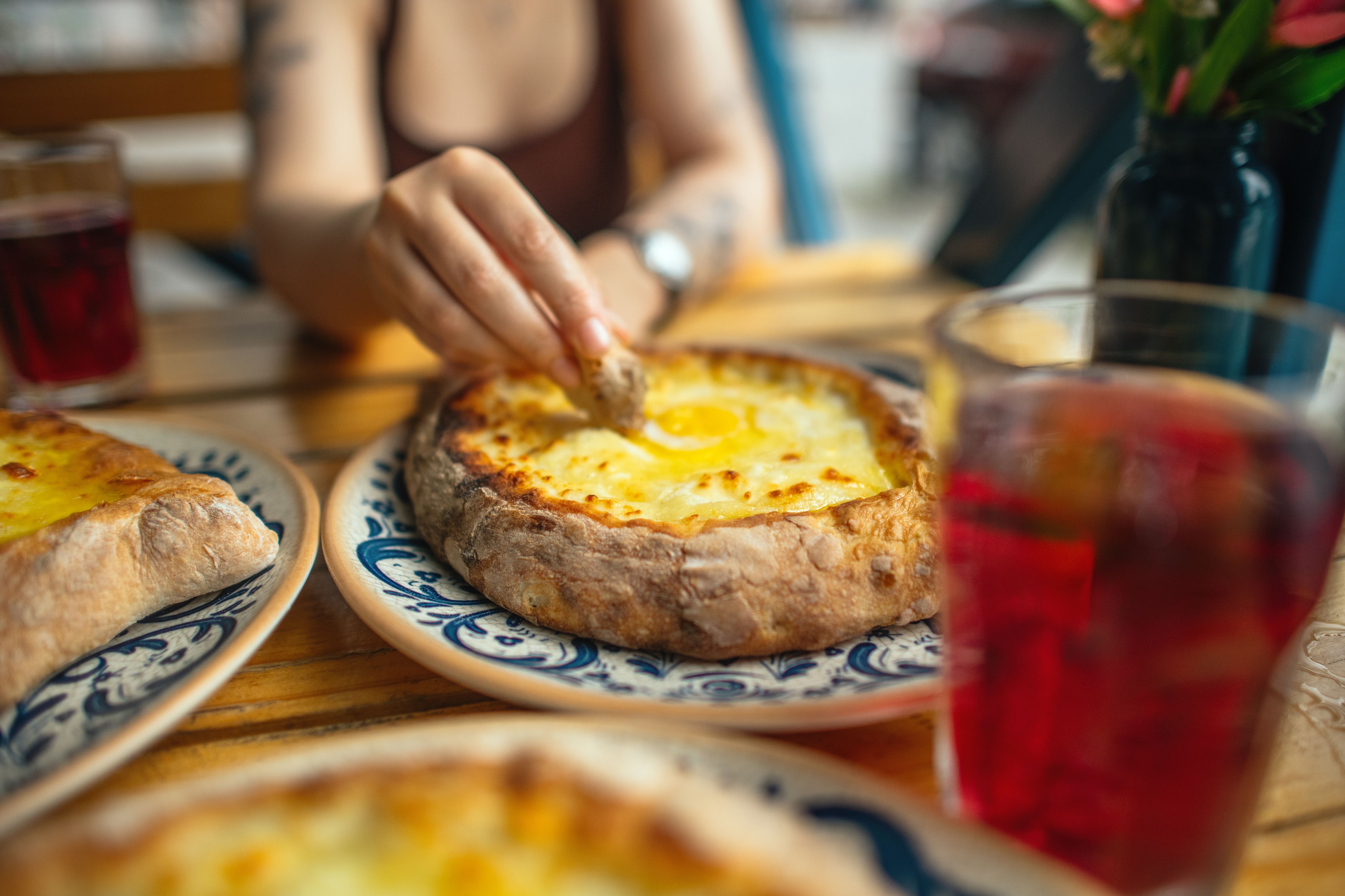 Woman eating Adjarian khachapuri with cheese, egg and butter, and soda drink. Traditional Georgian cuisine.