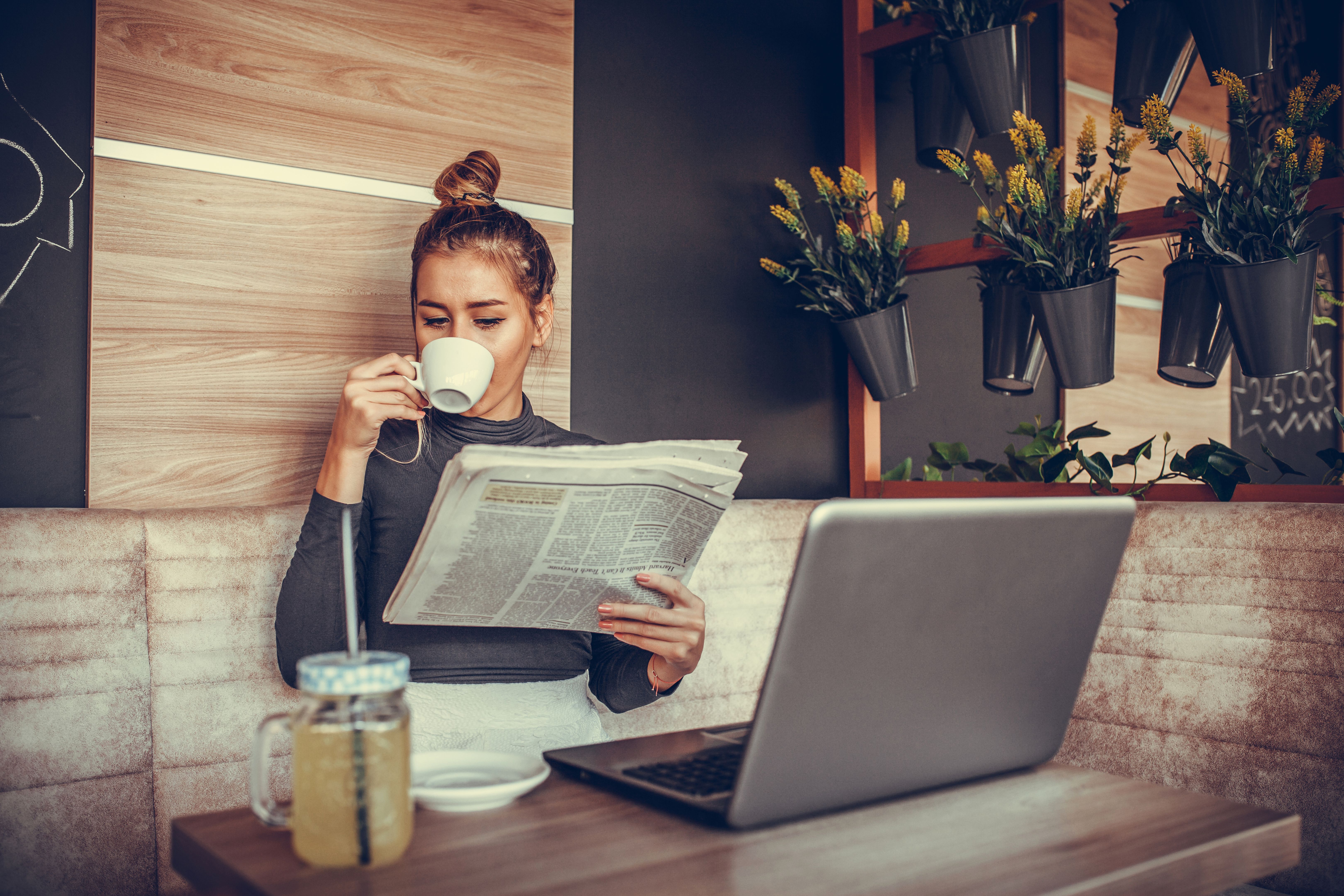 Beautiful young woman reading newspaper and drinking coffee in coffee shop Beautiful young woman reading newspaper and drinking coffee in coffee shop