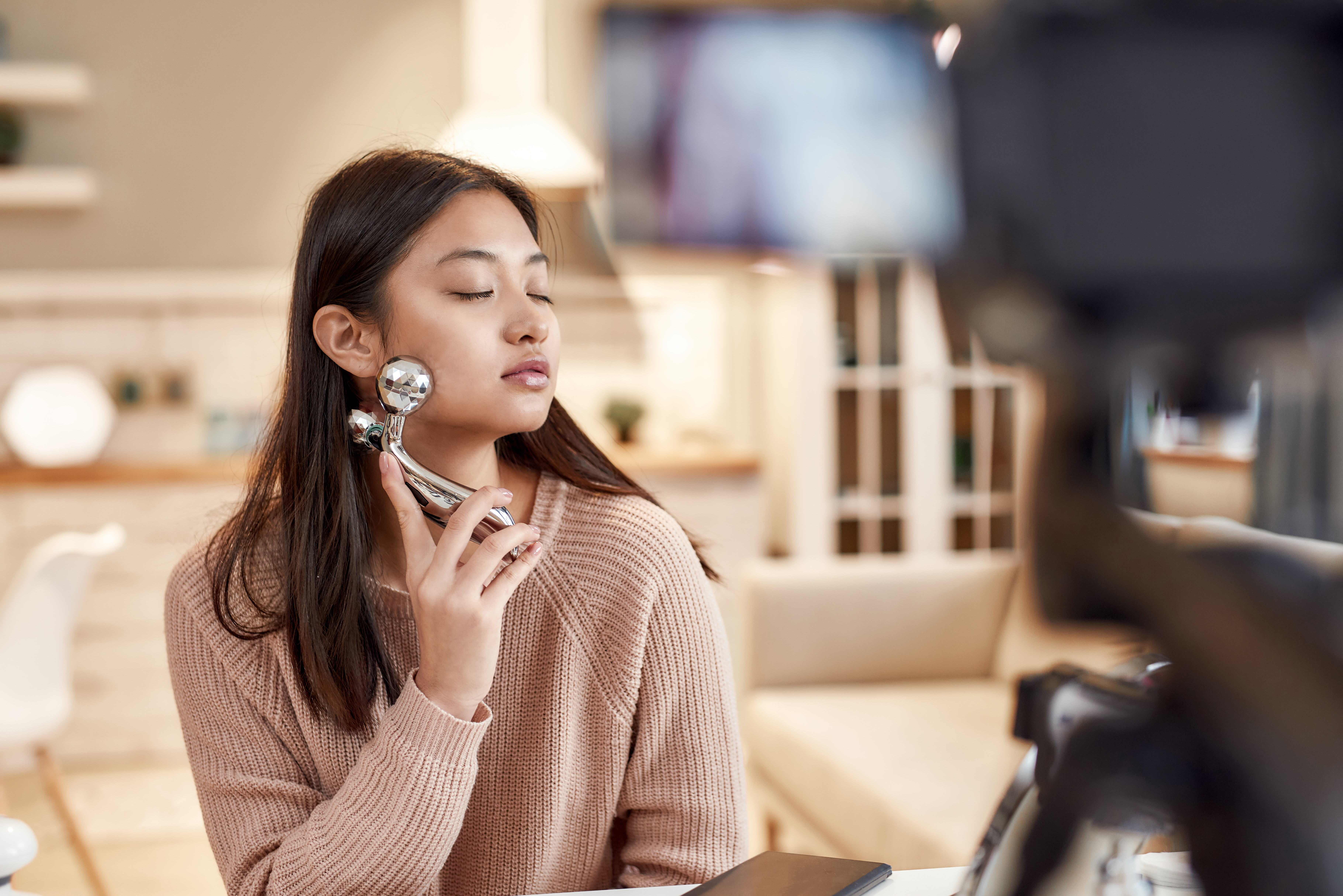 Skincare routine. Young female blogger massaging her face with facial roller while recording a video for her beauty blog. Face lift, anti aging treatment concept