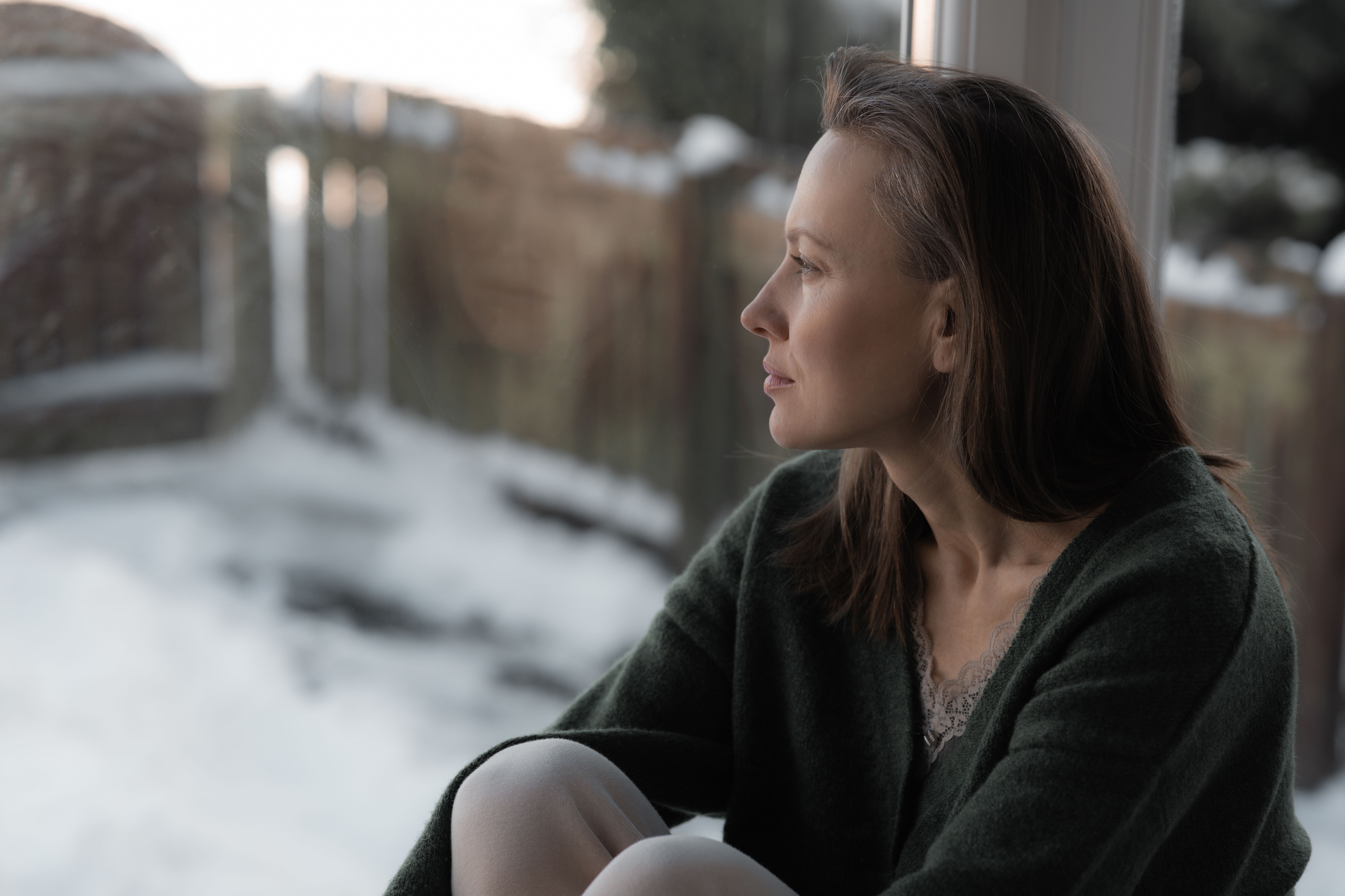 Thoughtful sad woman sitting on a windowsill Thoughtful sad woman sitting on a windowsill