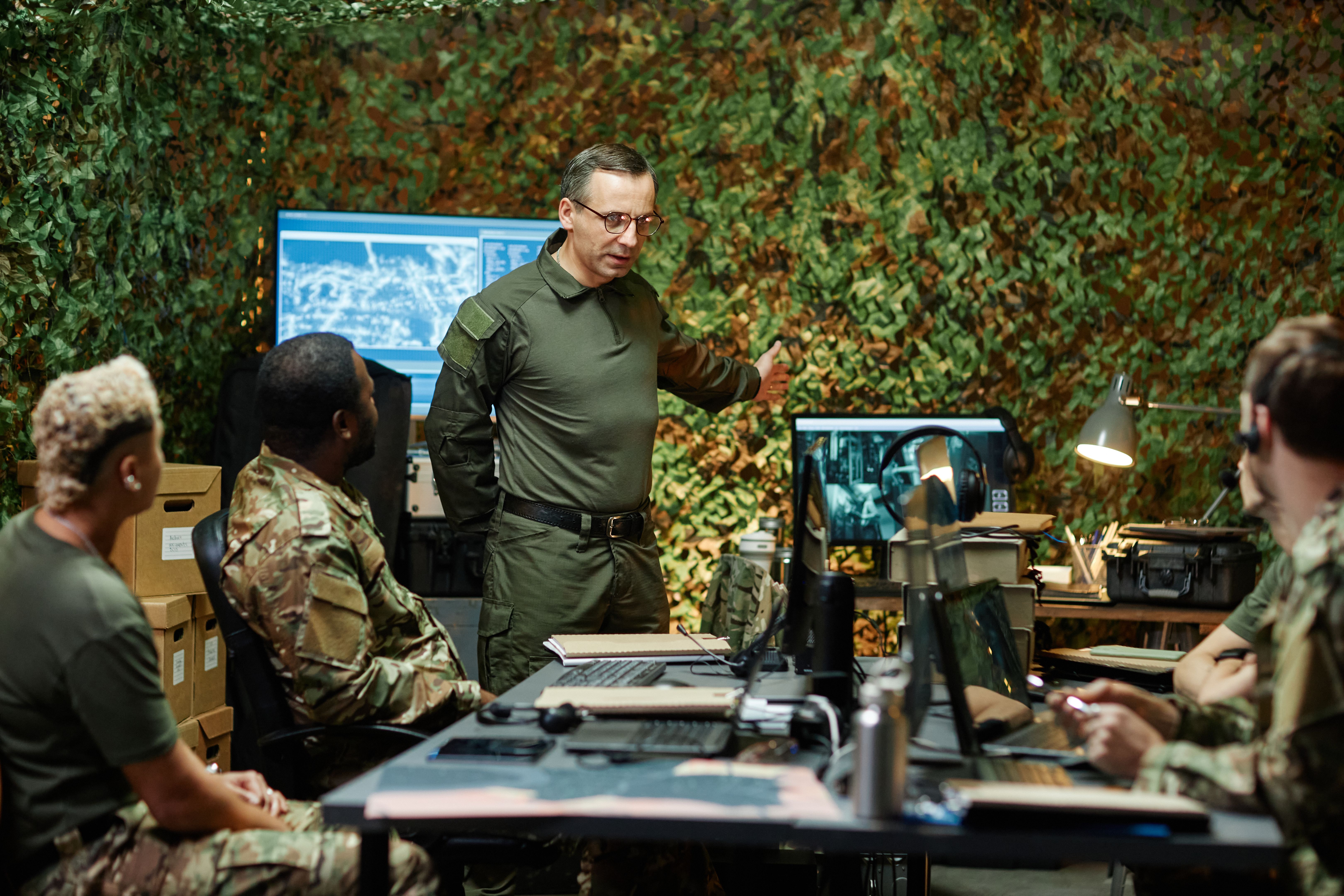 Confident man in uniform pointing at computer screen and explaining something