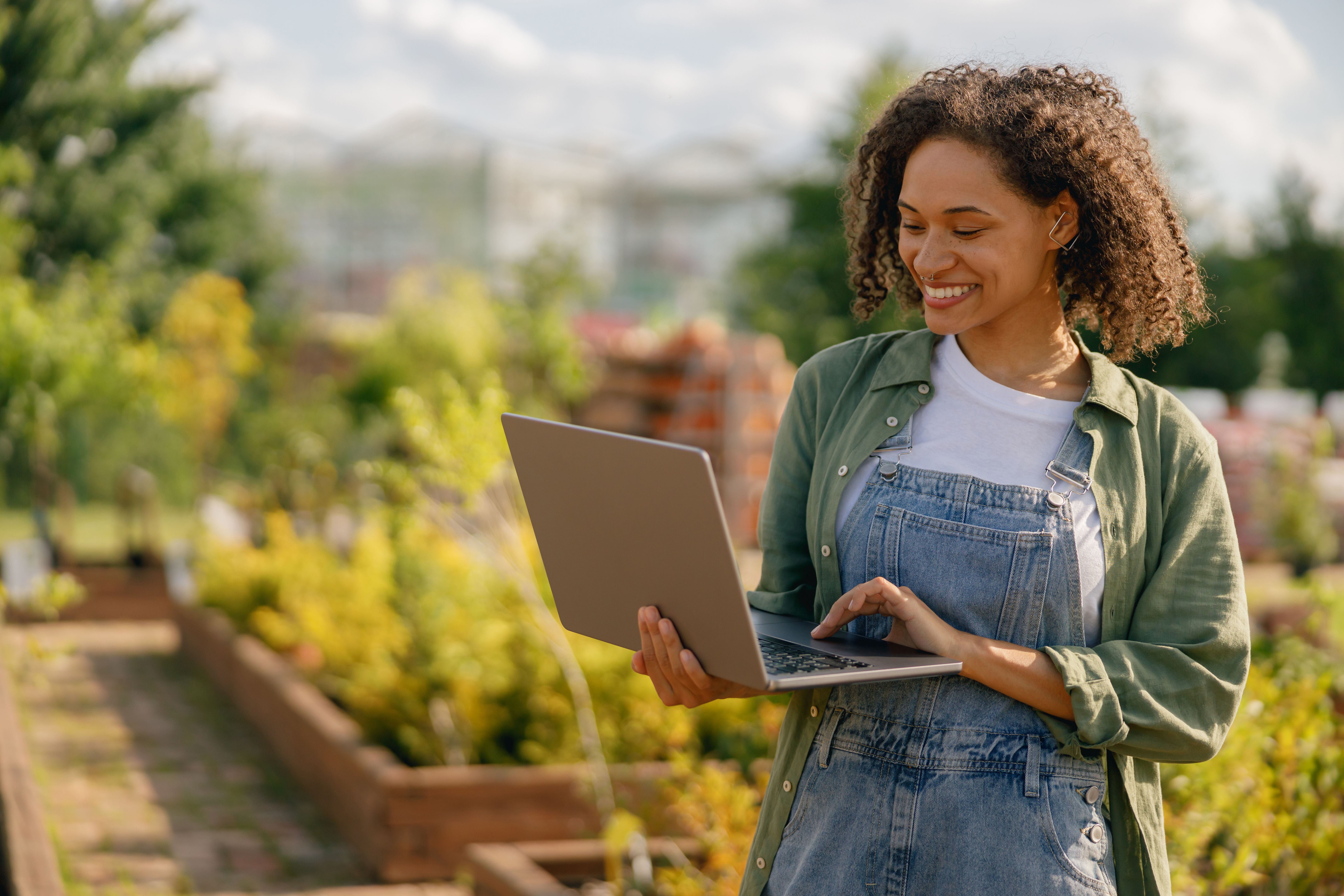 Cheerful woman gardener working on laptop while sitting on background of shop plants center
