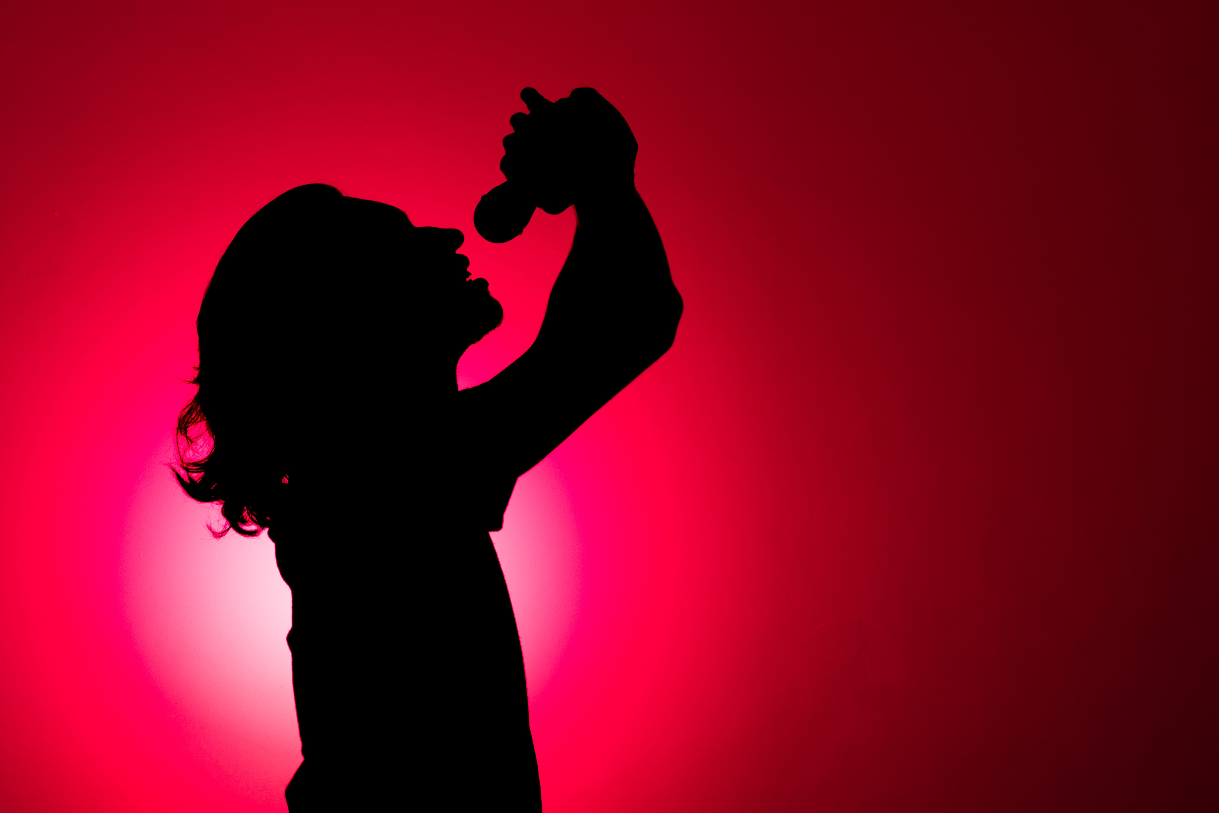 Silhouette of young man holding wireless microphone and singing music with emotion.
