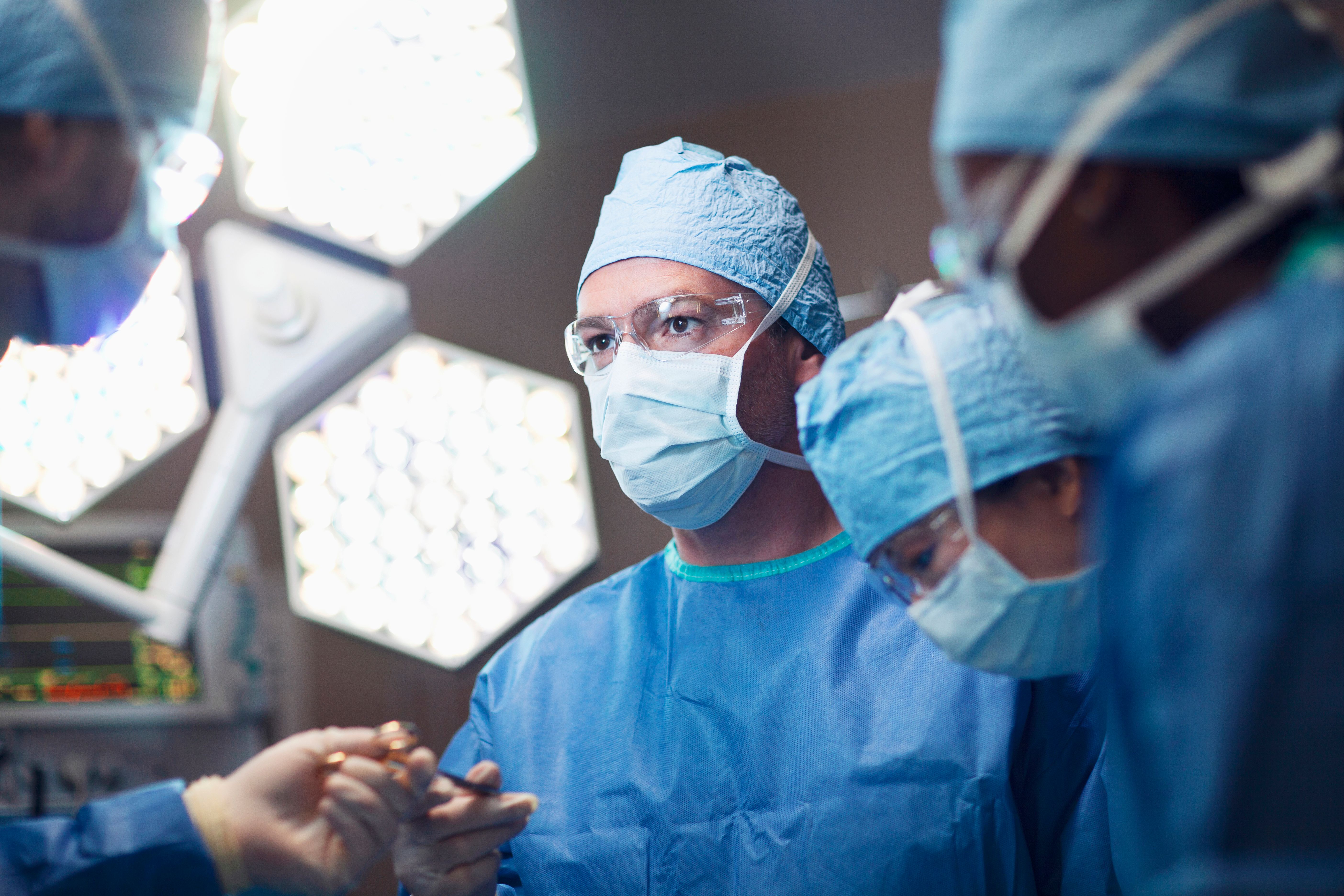 Middle Eastern multiracial mid adult man doctor surgeon nurse passing medical tool in surgery operating room hospital with medical team