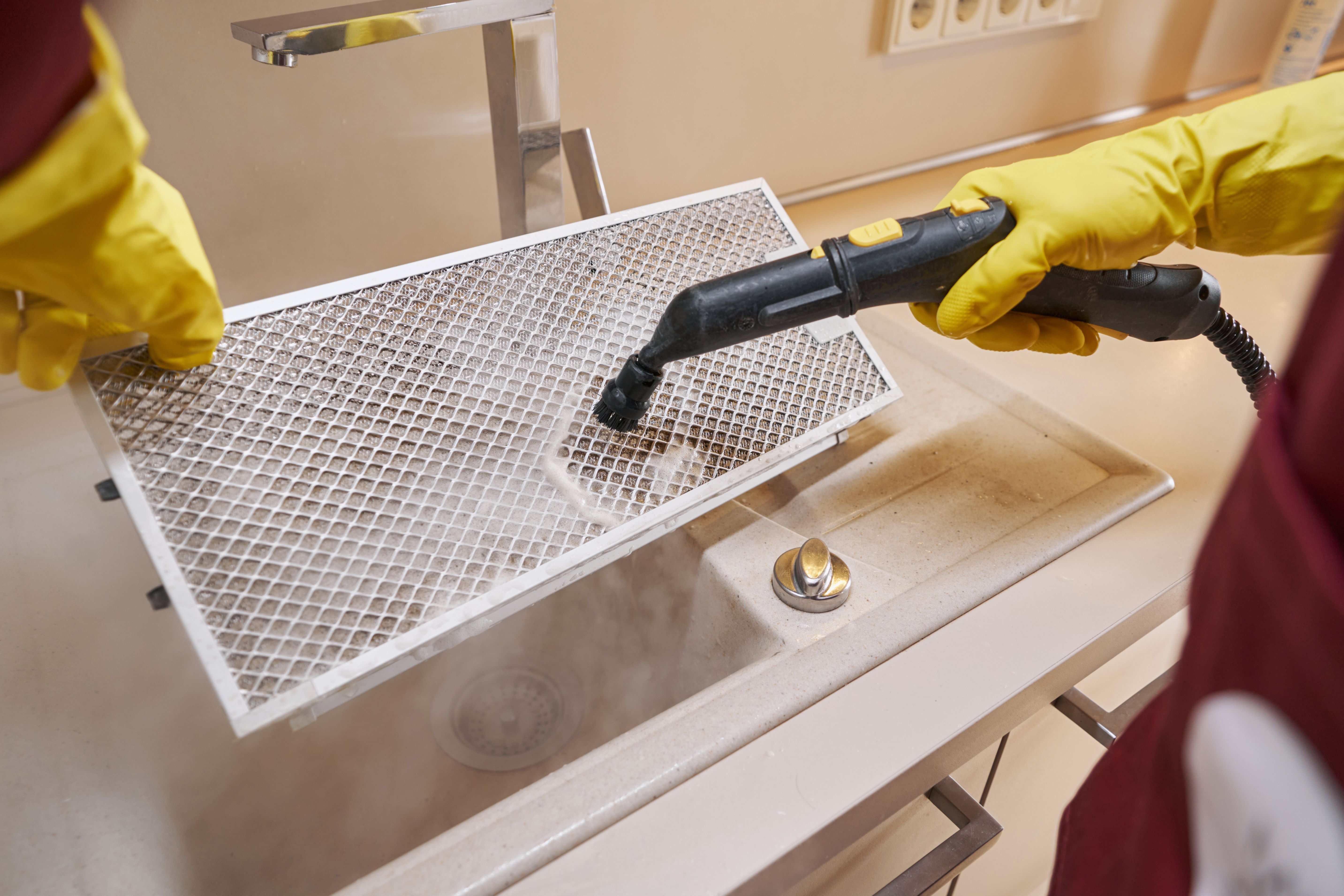 Cleaning person disinfecting kitchen air purifier part with steam cleaner Cleaning person disinfecting kitchen air purifier part with steam cleaner