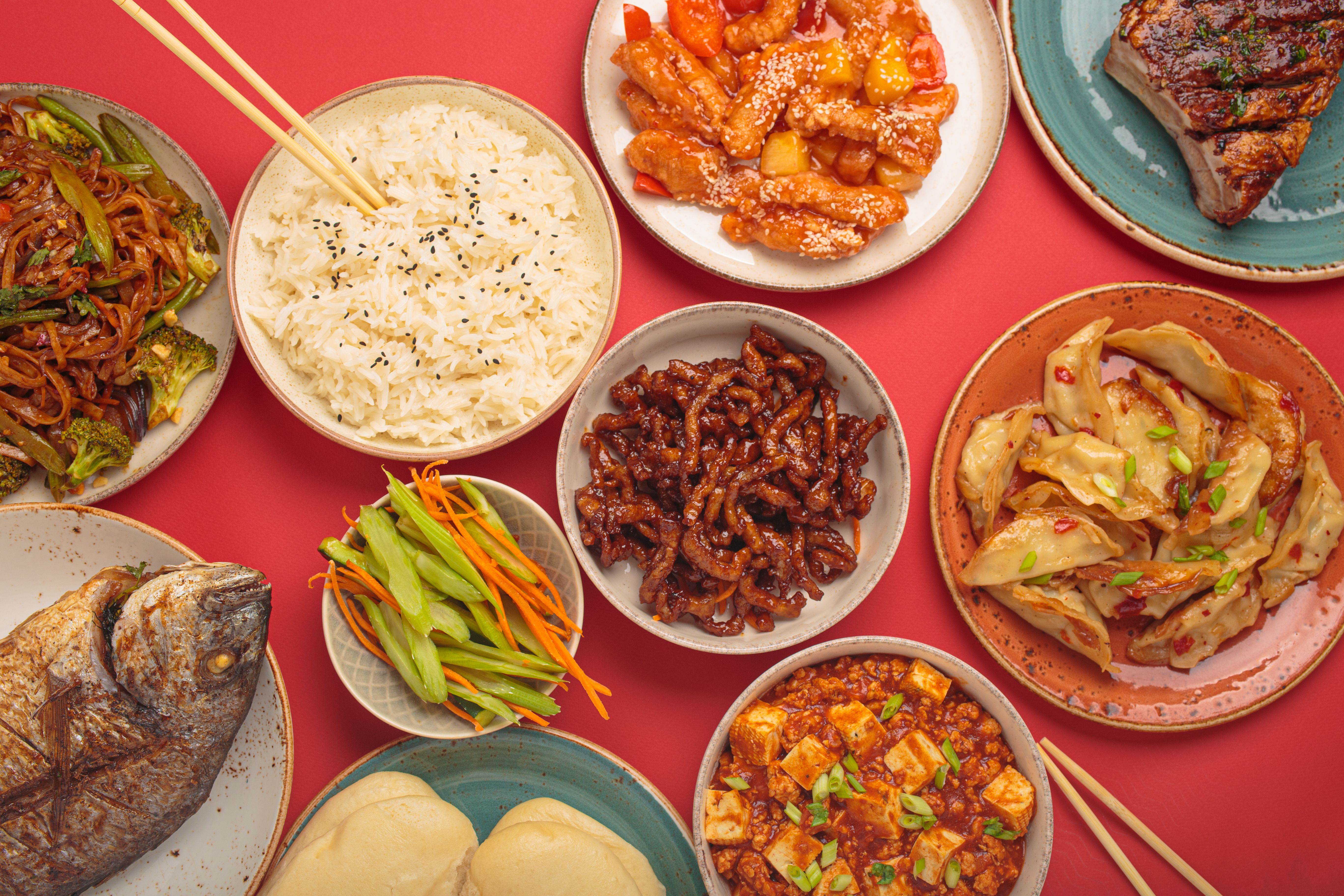 Assorted traditional  chinese dishes top view on red background: kung pal chicken, sweet and sour pork, noodles, dumplings, mapo tofu, fish, rice