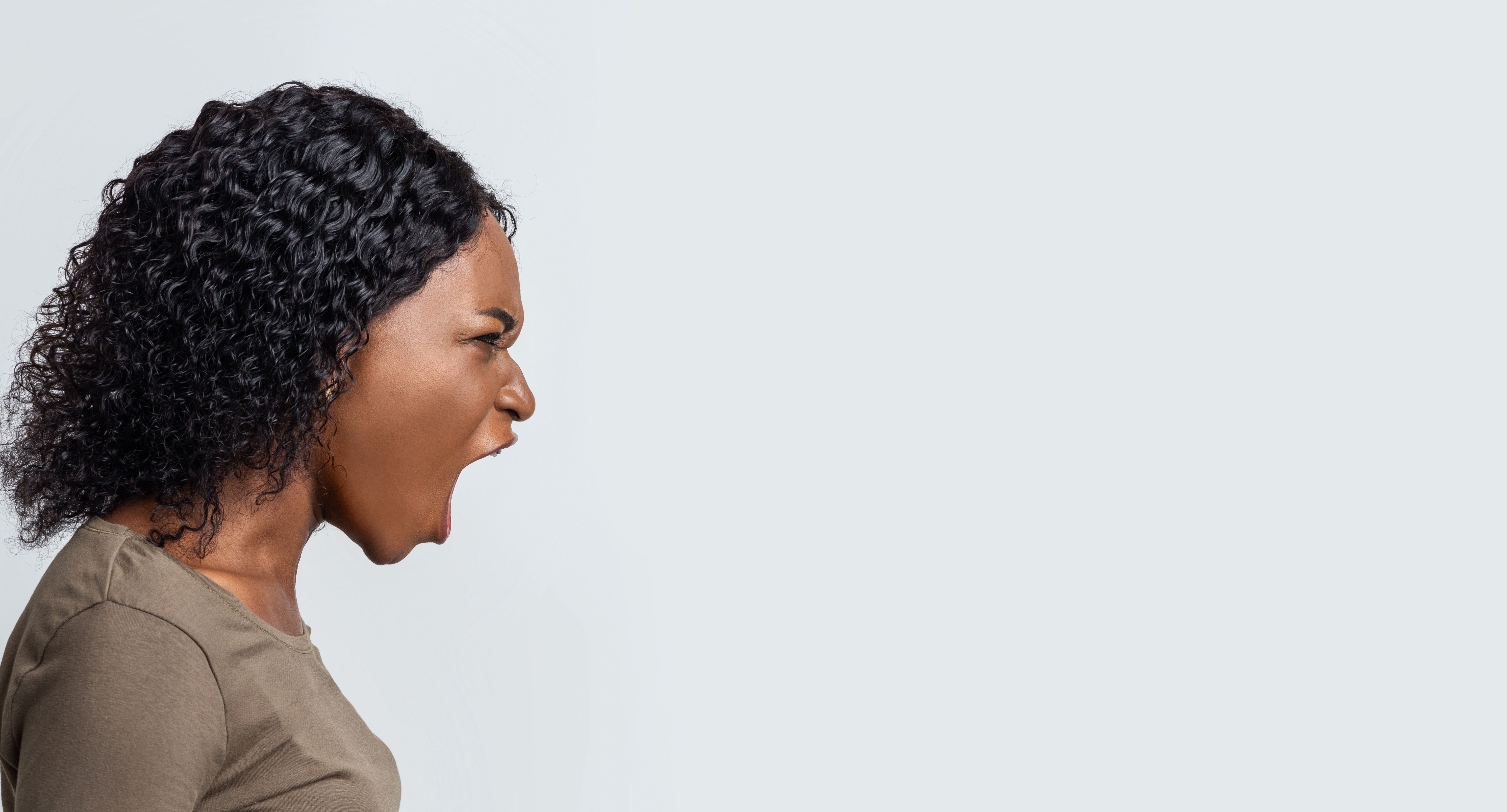 Angry black woman shouting towards copy space over grey background