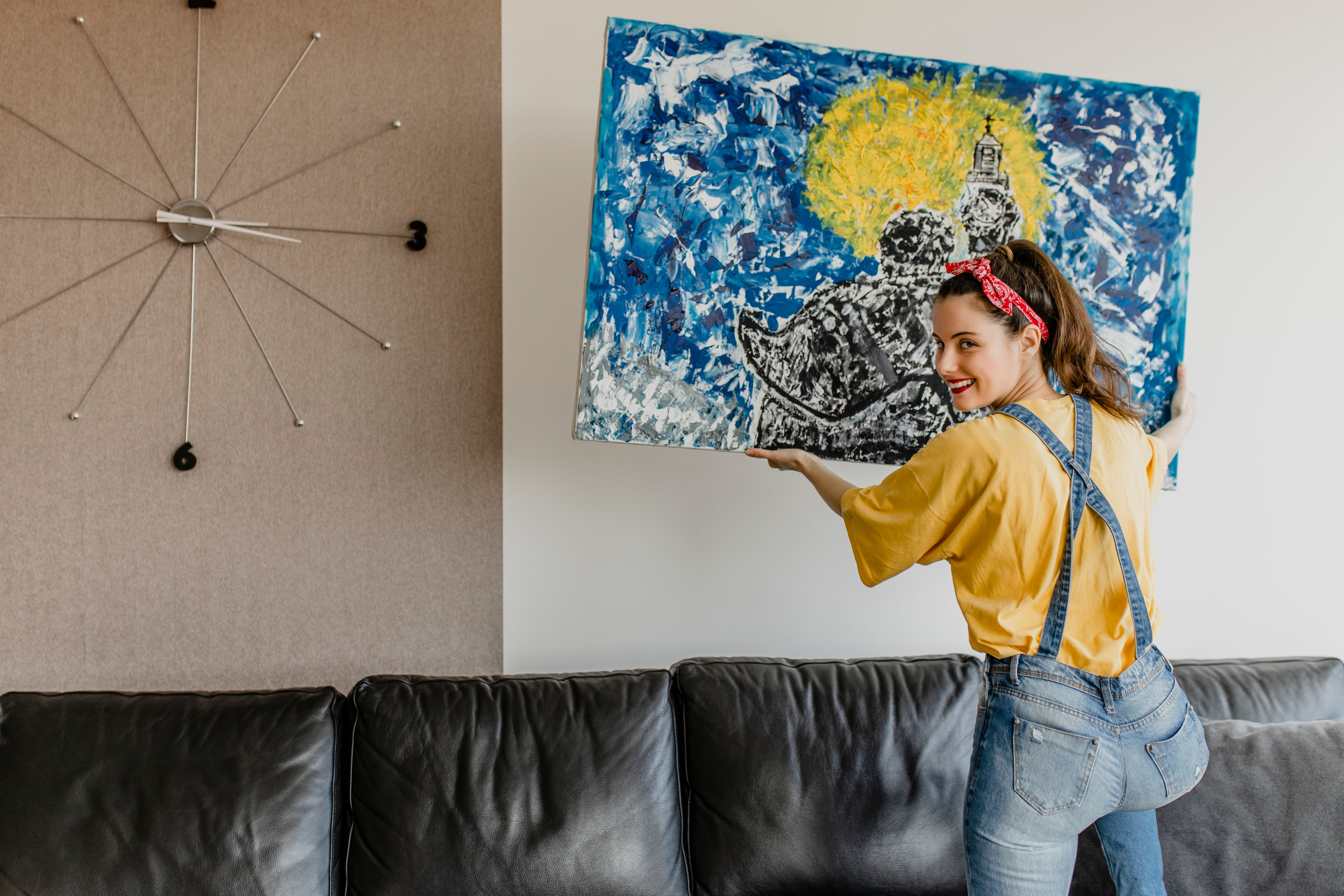 Young woman hanging art picture on wall and decorating living room