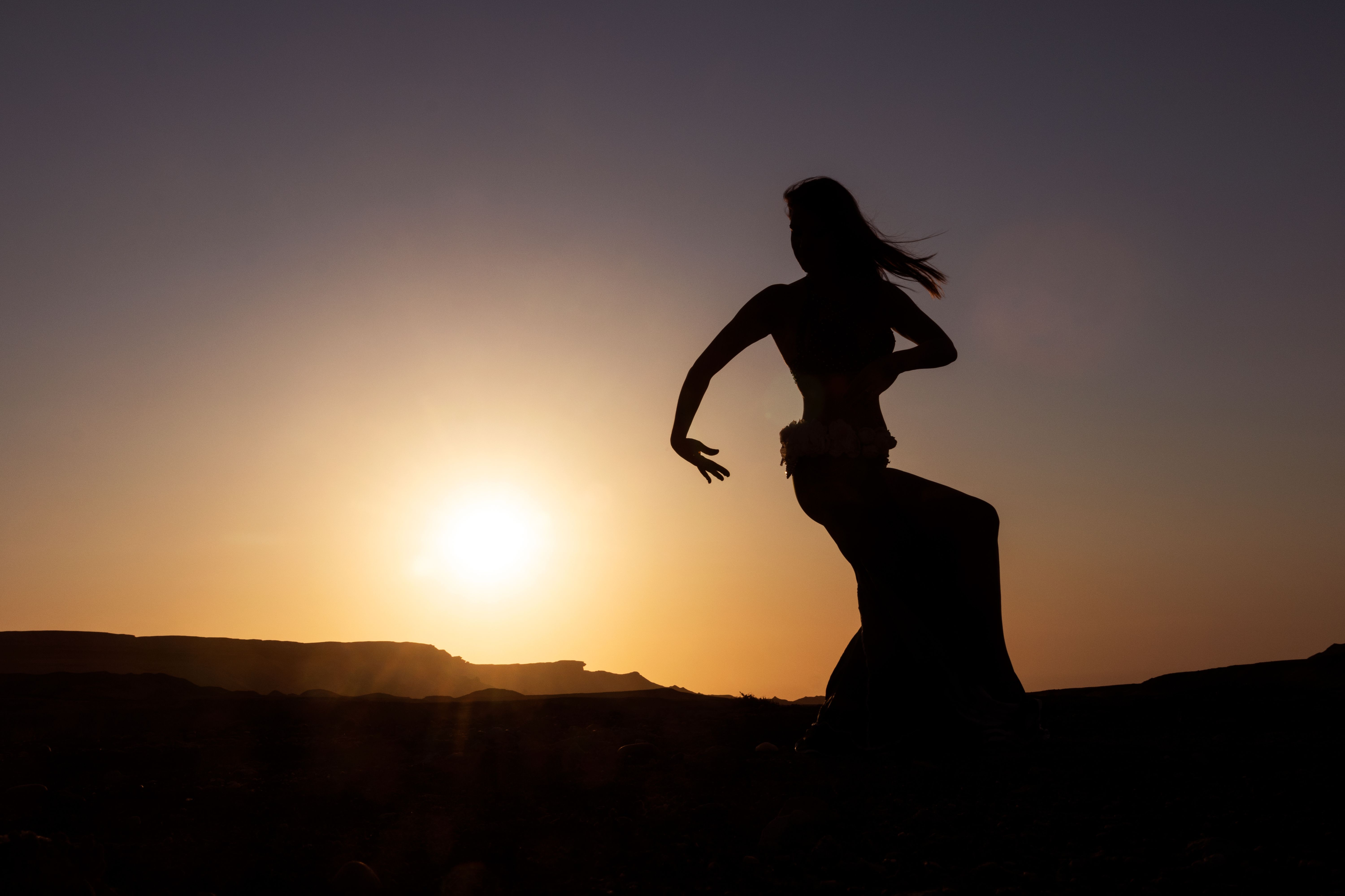 Silhouette of Woman dancing to the famous belly dance with sunset in the Namibe Desert with canyons. Africa. Angola. Silhouette of Woman dancing to the famous belly dance with sunset in the Namibe Desert with canyons. Africa. Angola.