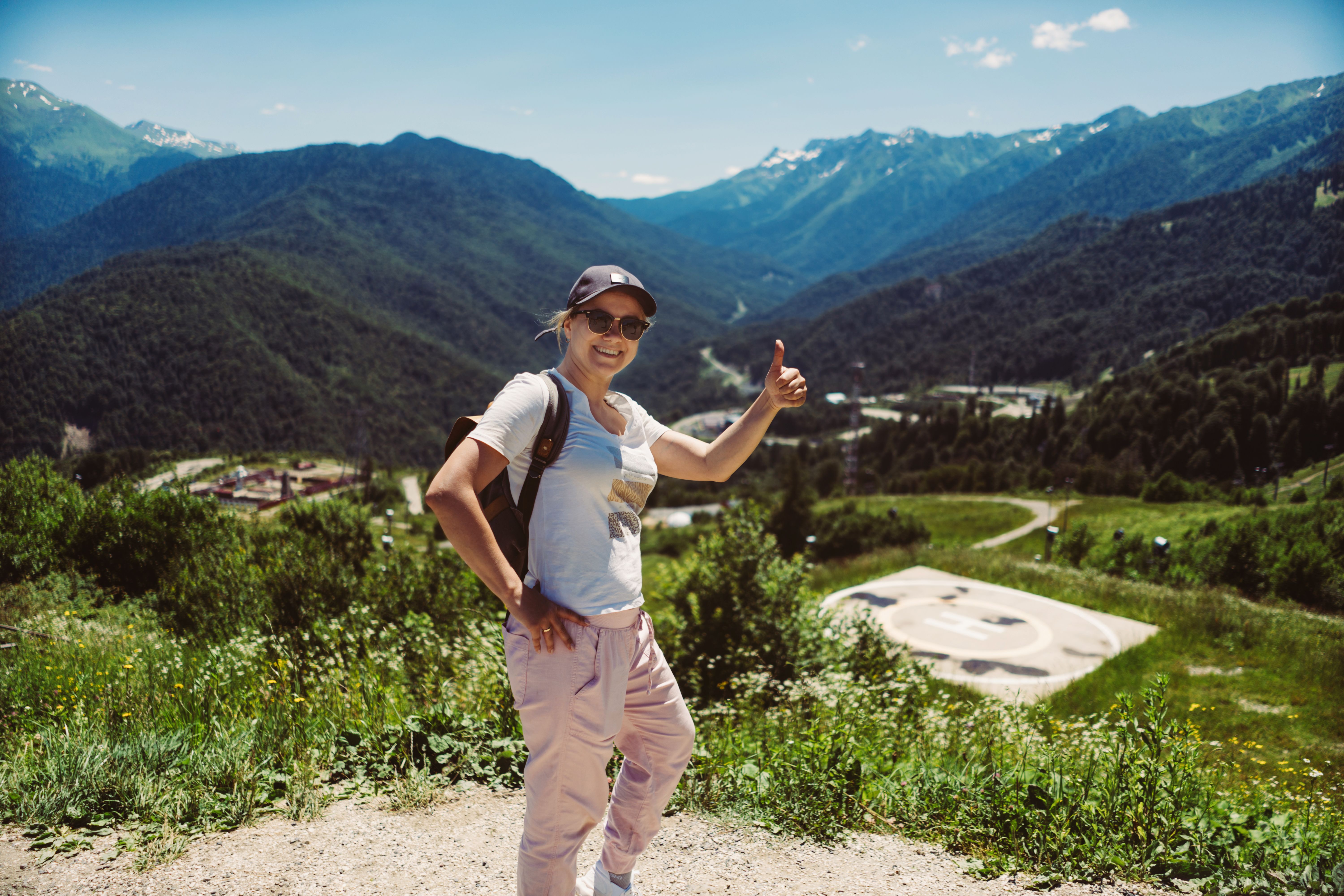 young stylish woman hiking alone with backpack enjoying beauty of mountains showing thumb up gesture