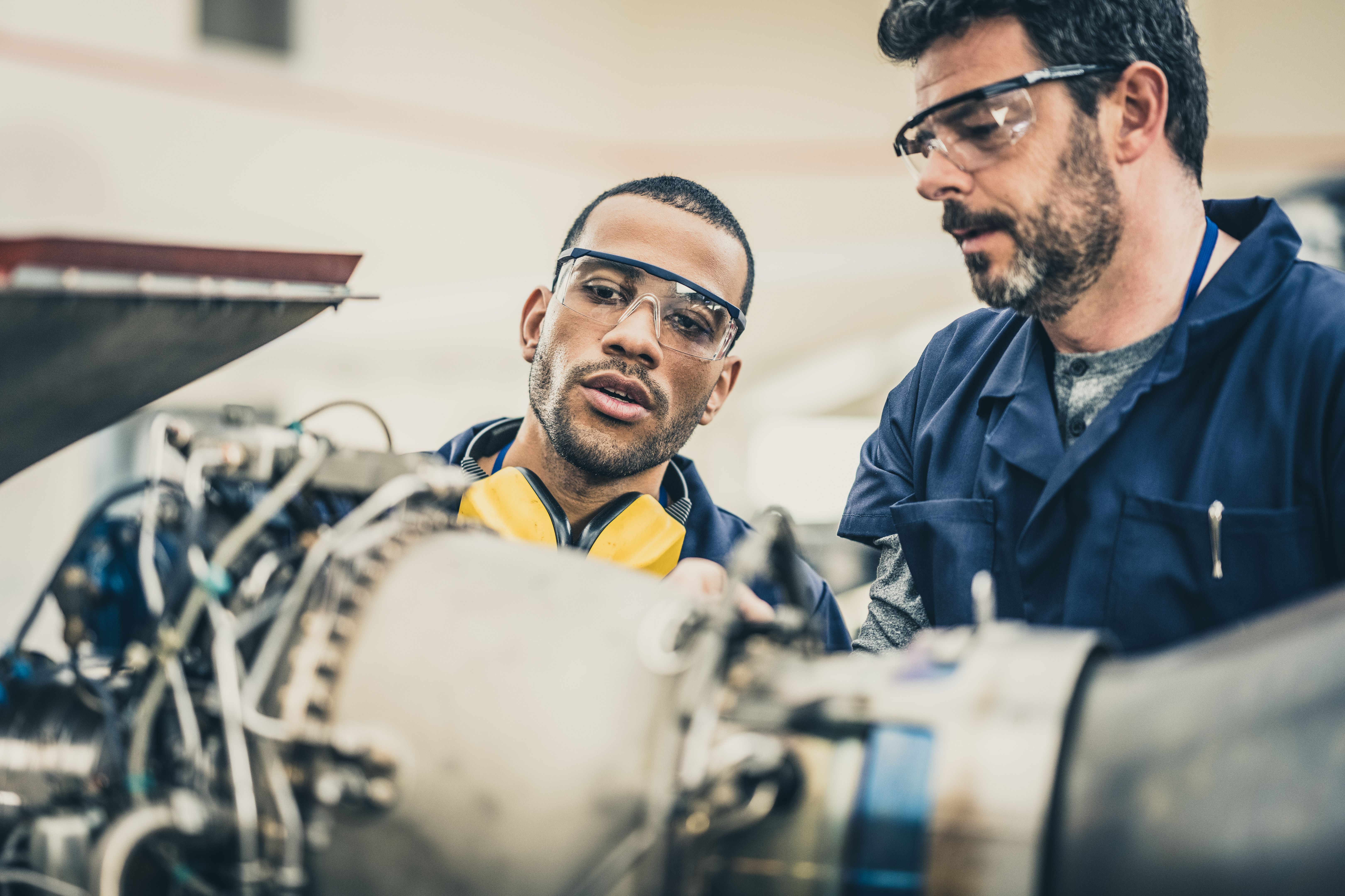 Aviation mechanic supervising young trainee and repairing helicopter turbine, close up Aviation mechanic supervising young trainee and repairing helicopter turbine, close up