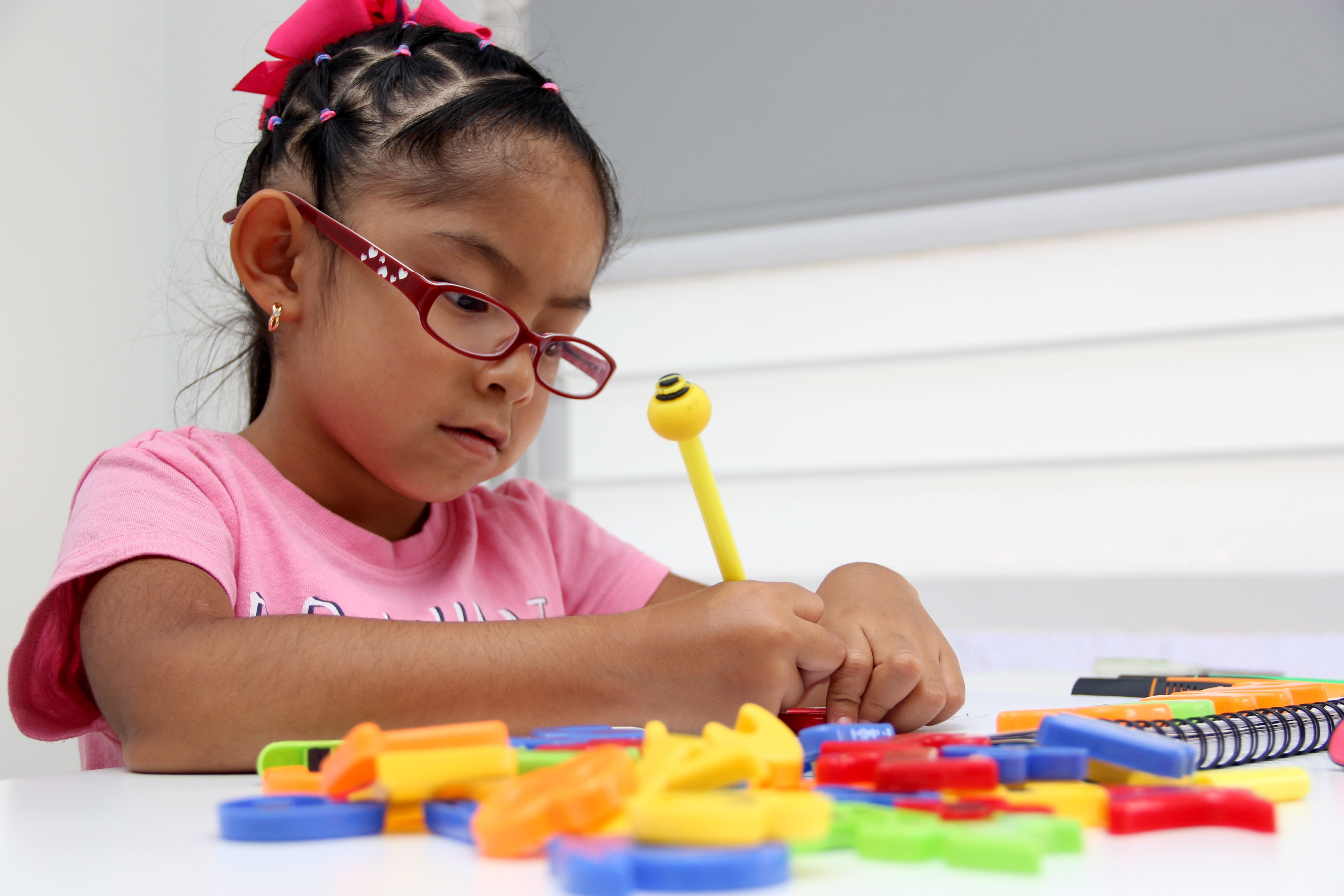 4-year-old brunette Latina girl with autism spectrum disorder ASD like Asperger, Rett and Heller draws at a desk, plays with colors antisocial