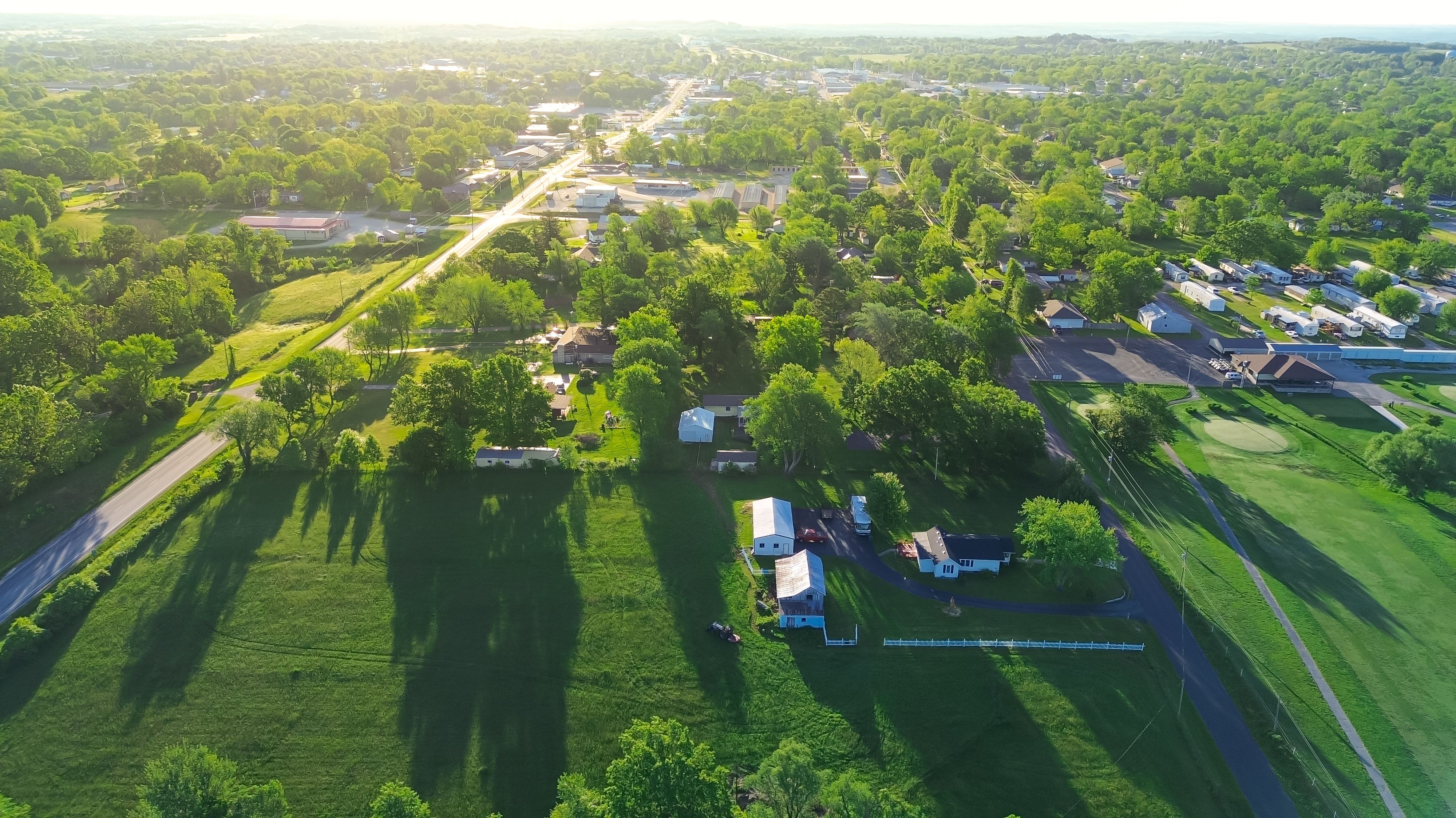 Service road with power line in countryside Mountain Grove Missouri thru lush greenery trees, meadows and farm houses with ponds in agricultural area, peaceful rural lots in Midwest, aerial view