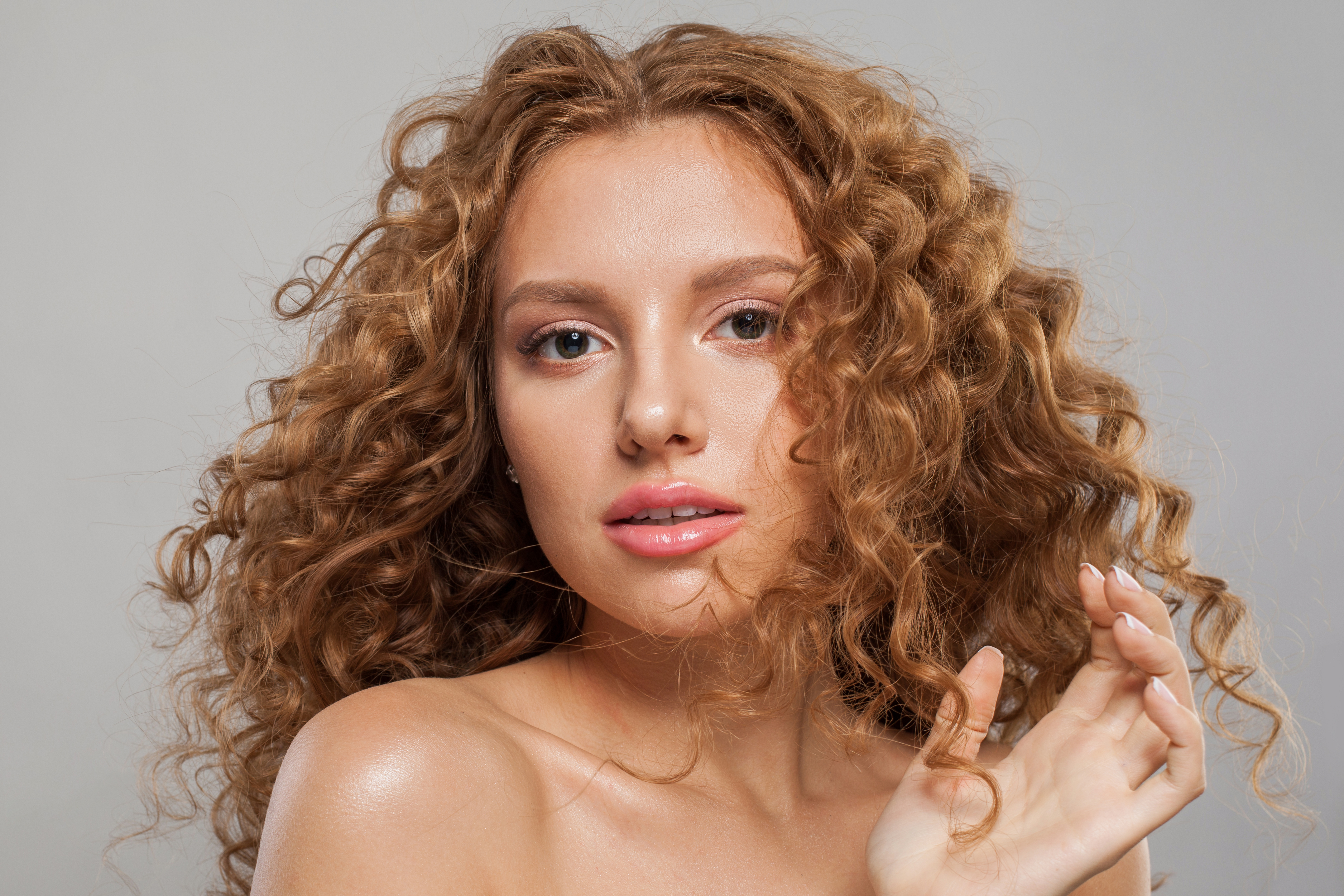 Attractive young female model healthy woman with long wavy frizzy hairstyle and clear skin studio portrait. Hair care, facial treatment and cosmetology concept Attractive young female model healthy woman with long wavy frizzy hairstyle and clear skin studio portrait. Hair care, facial treatment and cosmetology concept