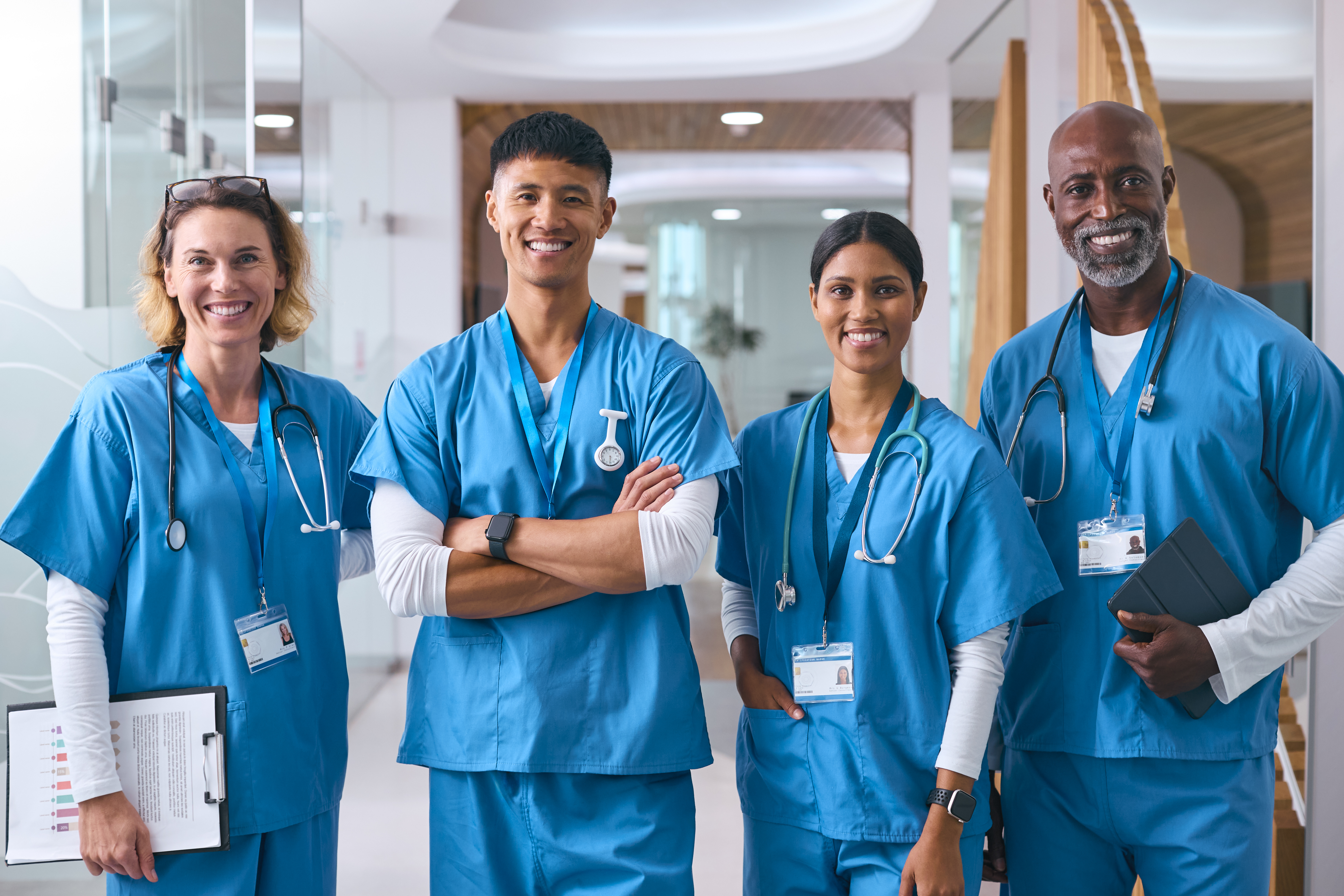 Portrait Of Smiling Multi Cultural Medical Team Wearing Scrubs In Modern Hospital
