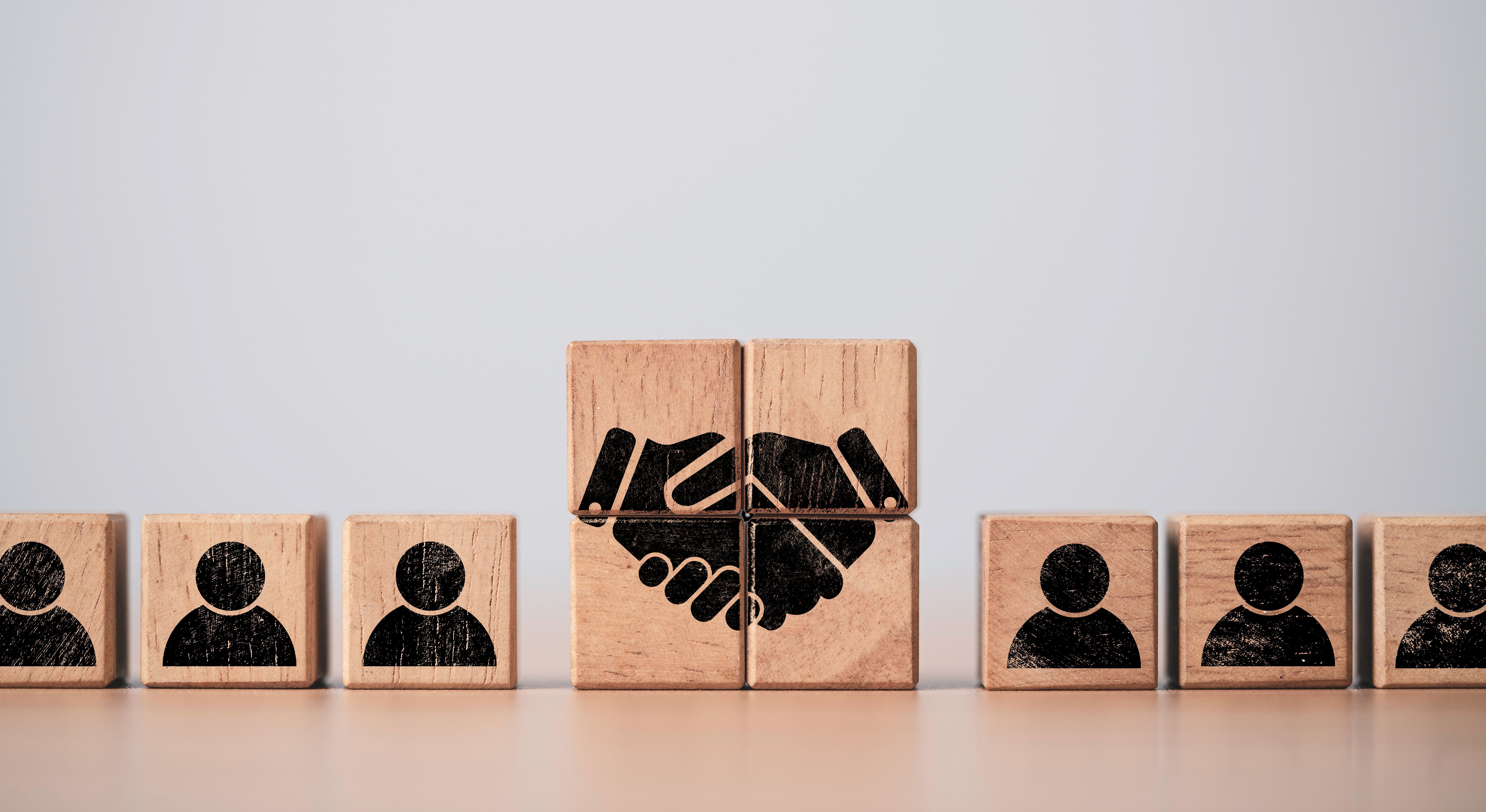 Hand shaking print screen on wooden block cube between human icon for business deal and agreement concept.