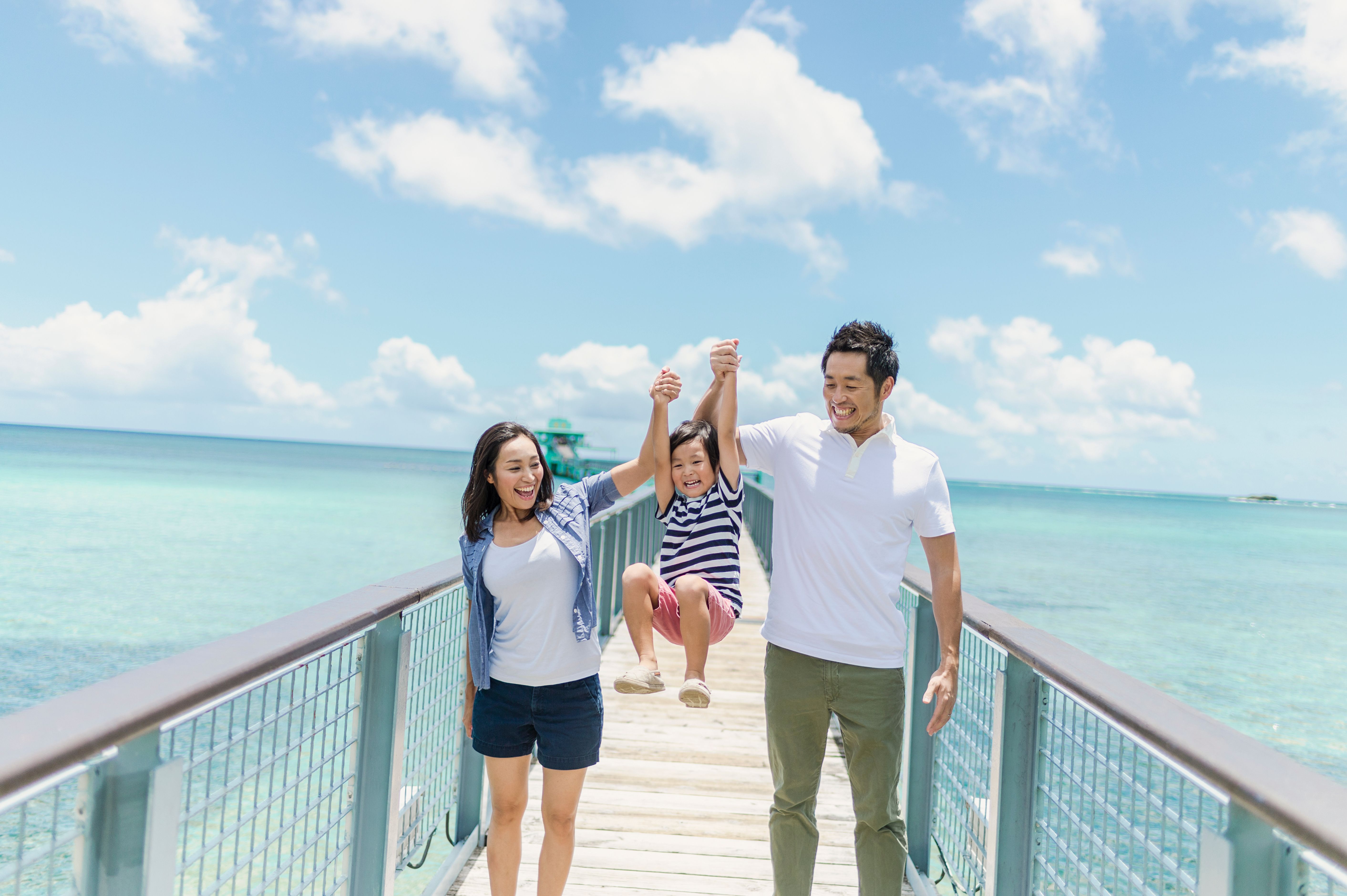 Japanese couple with small child walking on vacation with the ocean in the background Japanese couple with small child walking on vacation with the ocean in the background