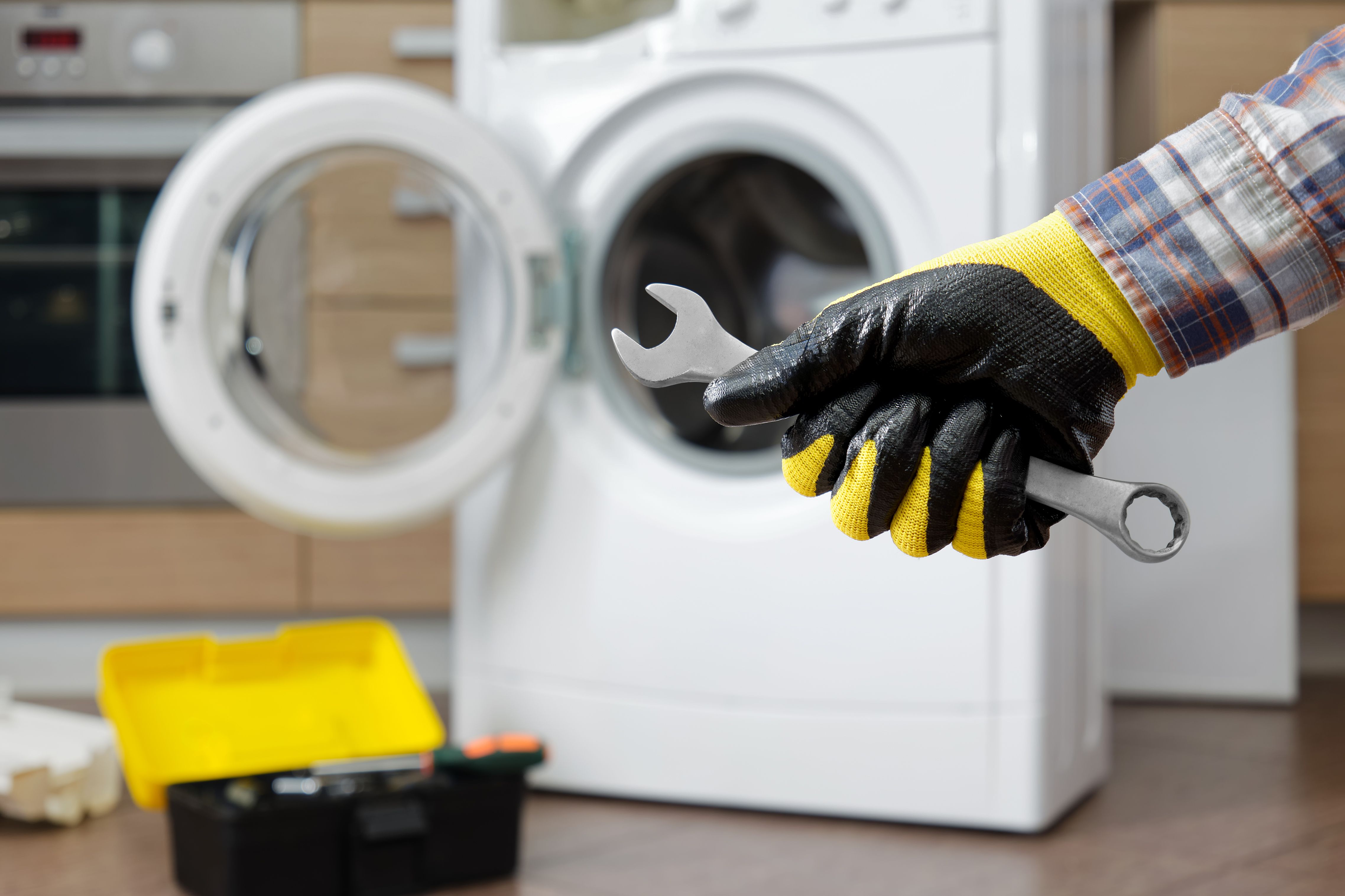 Close-up a hand a household appliance repairman with wrench against the backdrop of a domestic washing machine.