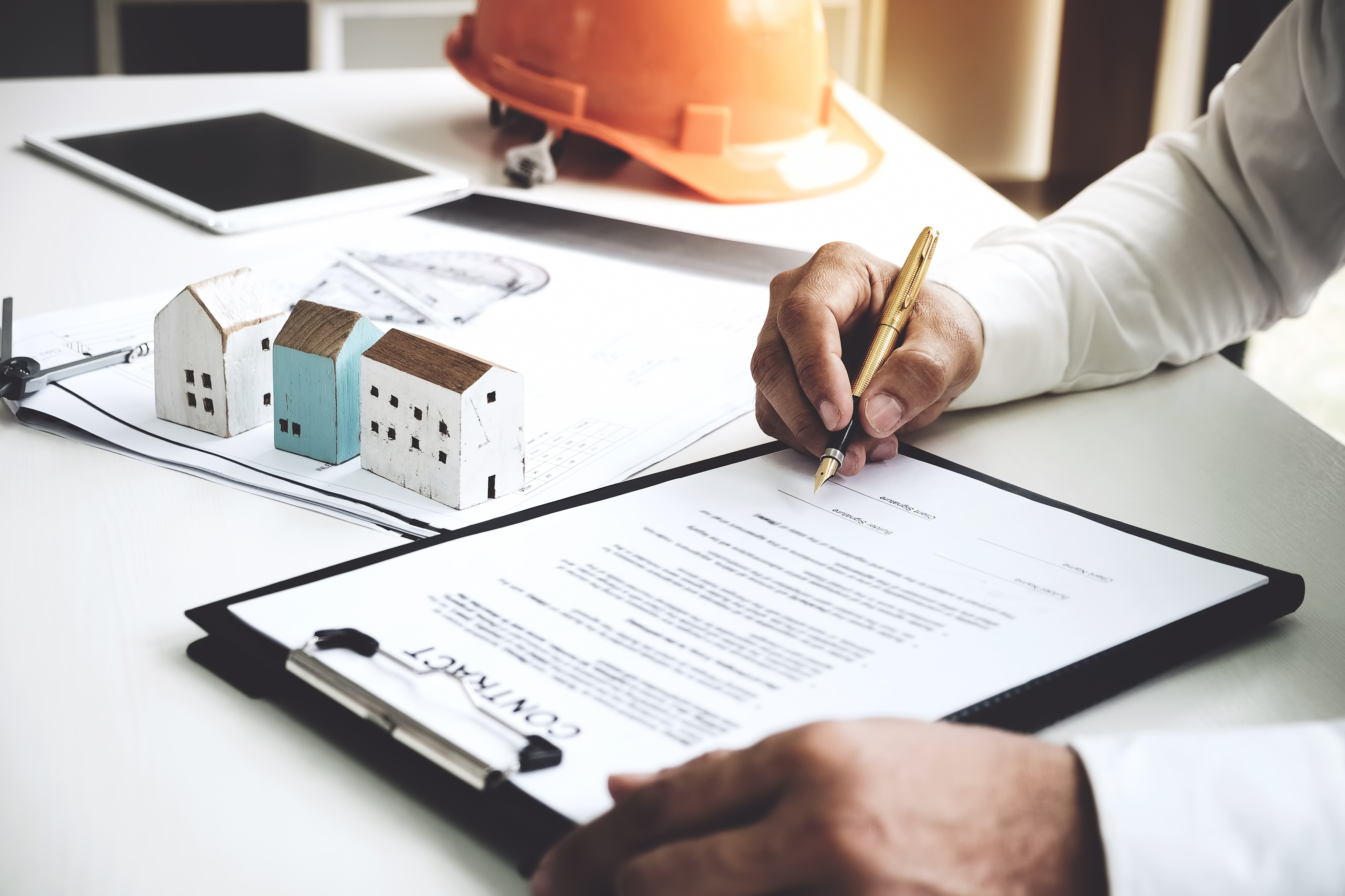 Businessmen are checking the contract to use the right pen. Signed building approval with blueprint and house model on the table.