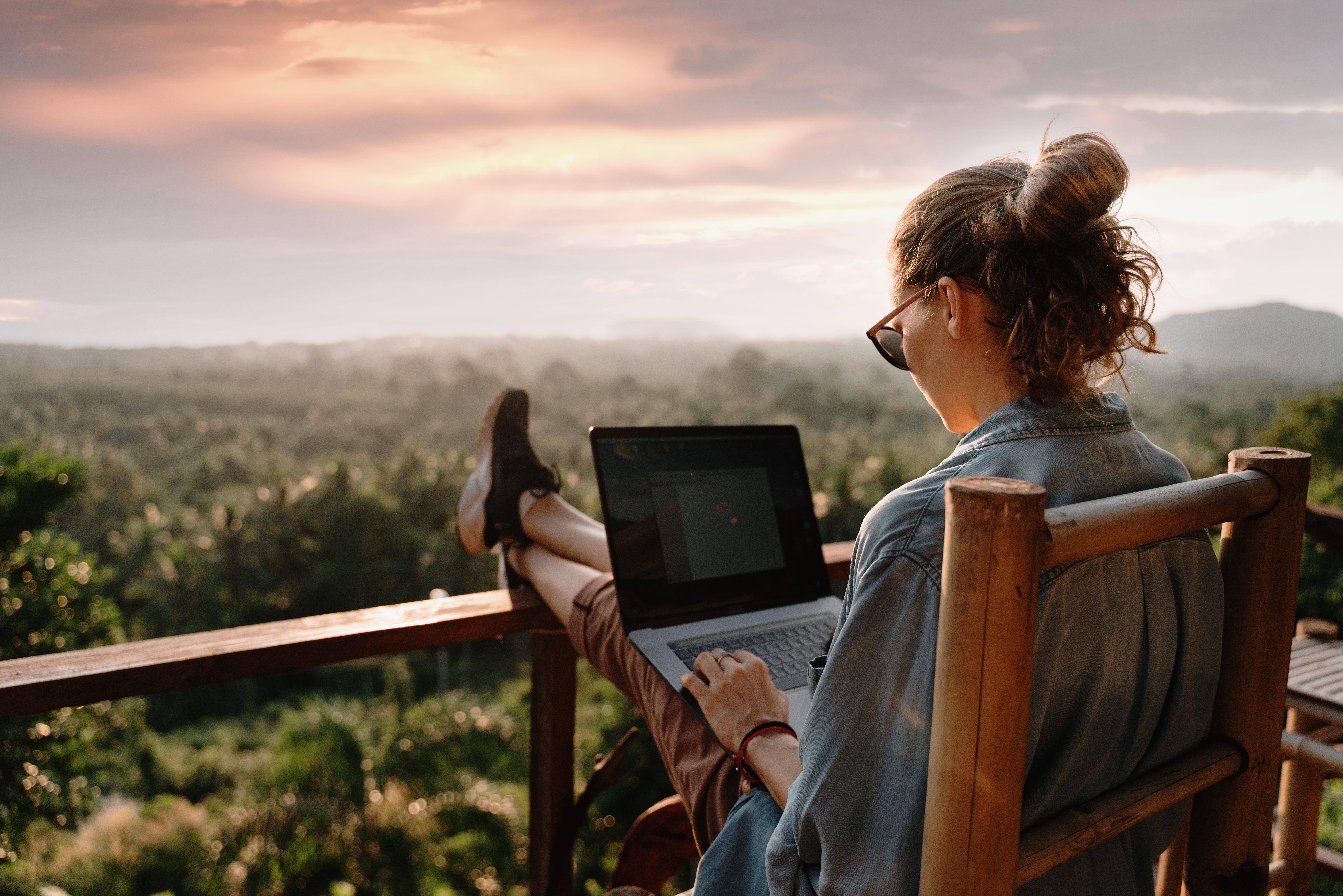 Young business woman working at the computer in cafe on the rock. Young girl downshifter working at a laptop at sunset or sunrise on the top of the mountain to the sea, working day. Young business woman working at the computer in cafe on the rock. Young girl downshifter working at a laptop at sunset or sunrise on the top of the mountain to the sea, working day.