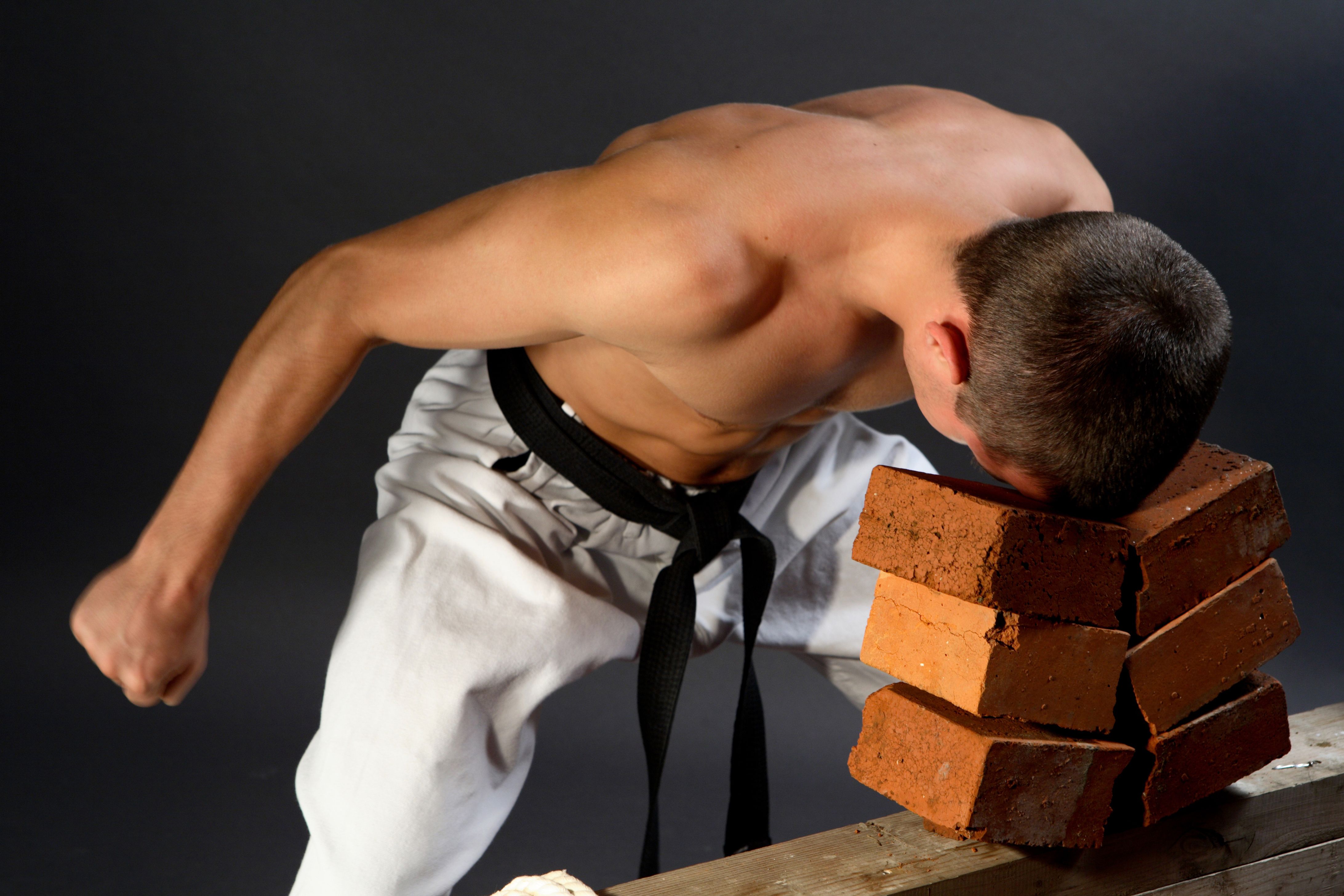 Young sporty karate man breaking three bricks on gray background