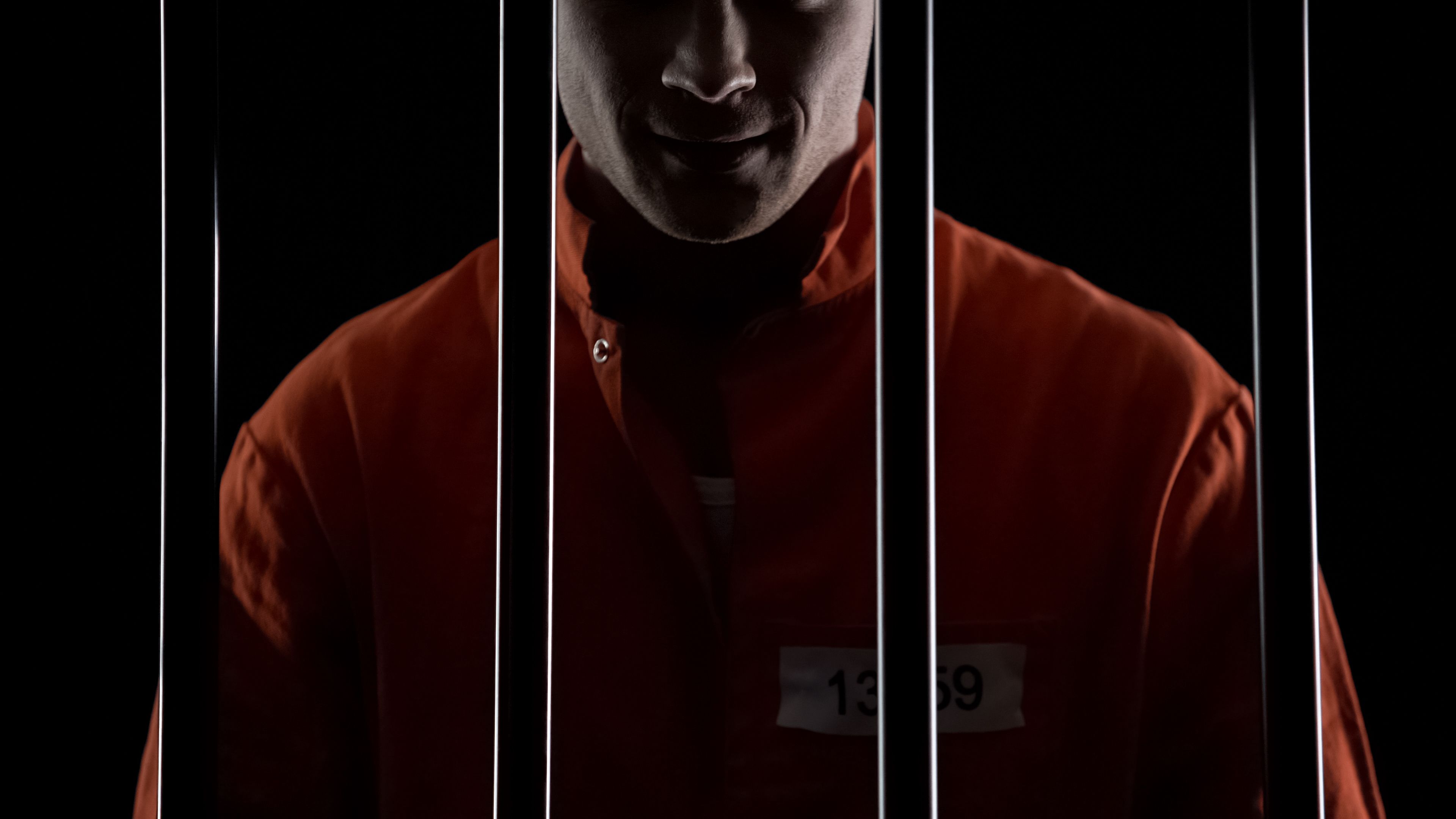 Mad serial killer standing behind prison bars and smirking, mental disorder