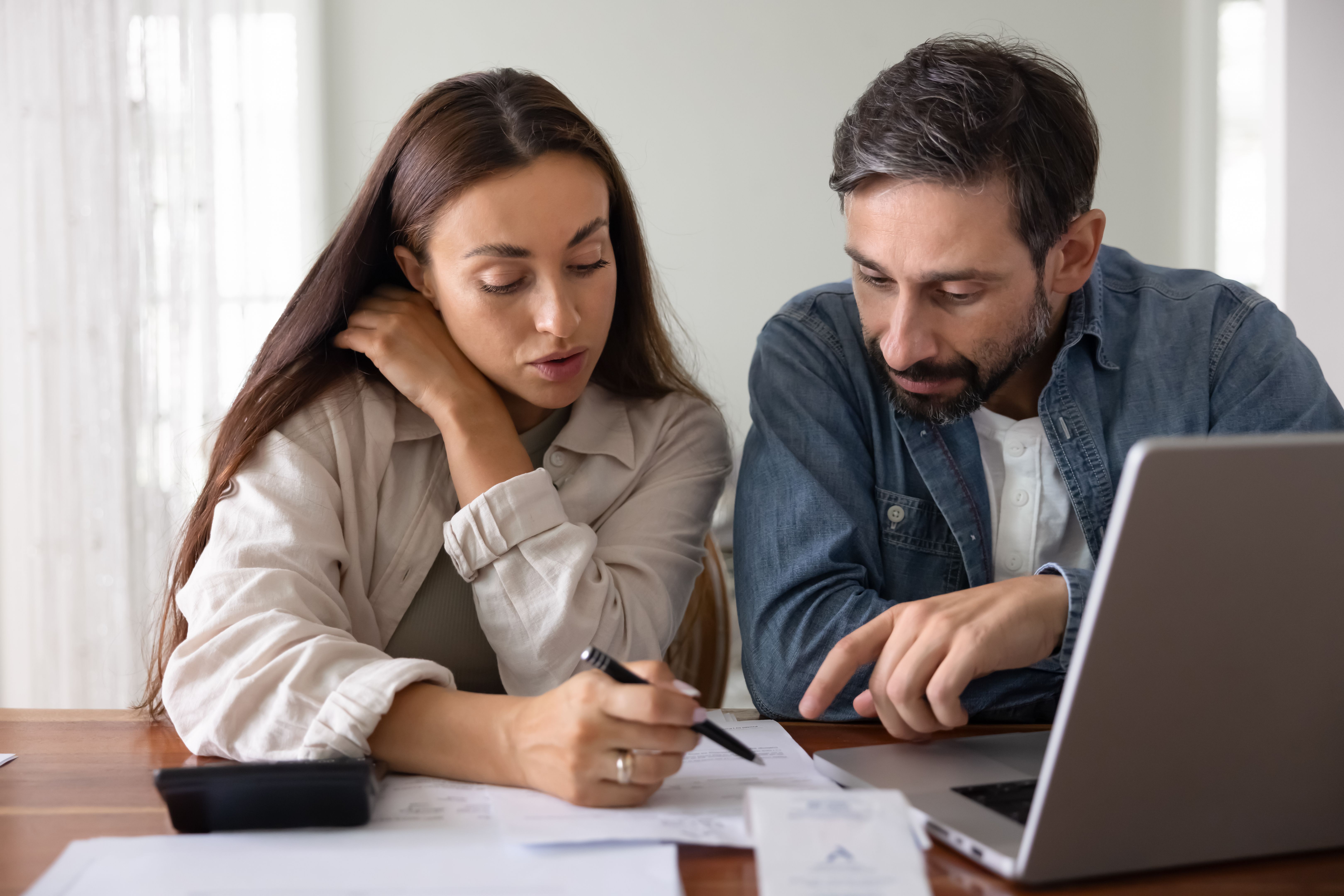 Un couple examine des documents financiers ensemble assis à une table avec un ordinateur portable Un couple examine des documents financiers ensemble assis à une table avec un ordinateur portable