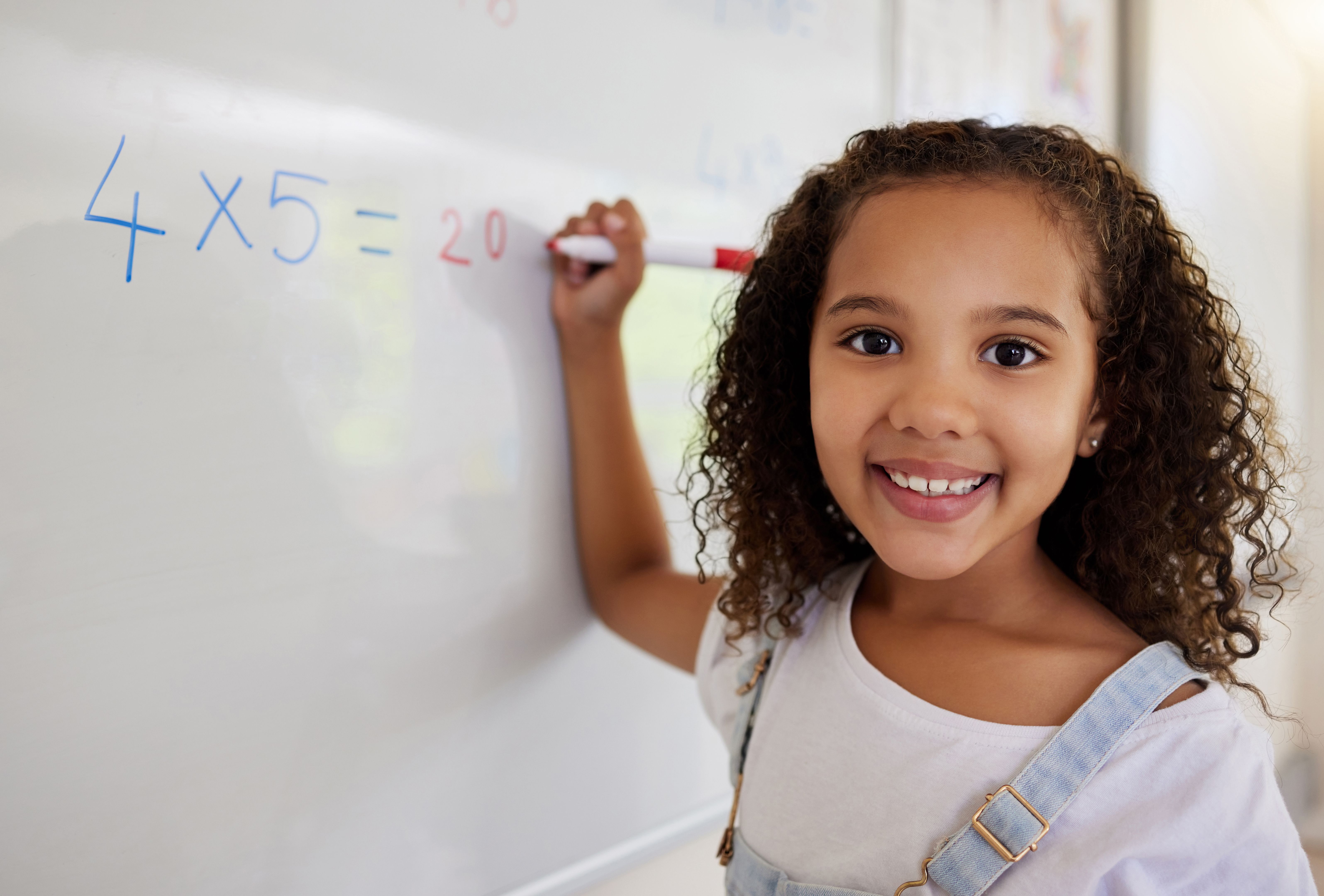 Shot of a little girl doing math's on a board in a  classroom