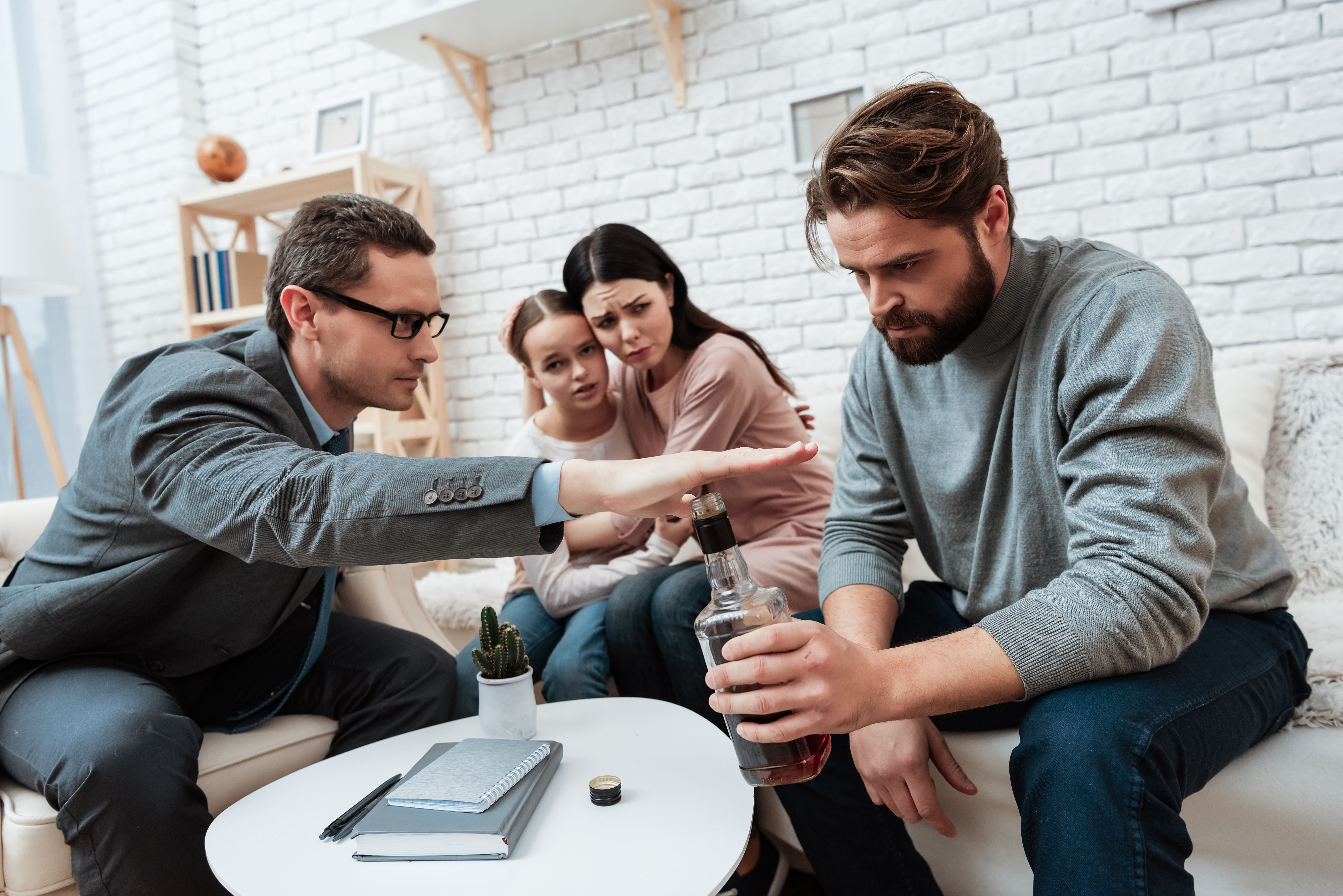Psychologist does not allow bearded man to drink alcohol, near which wife and daughter are sitting.