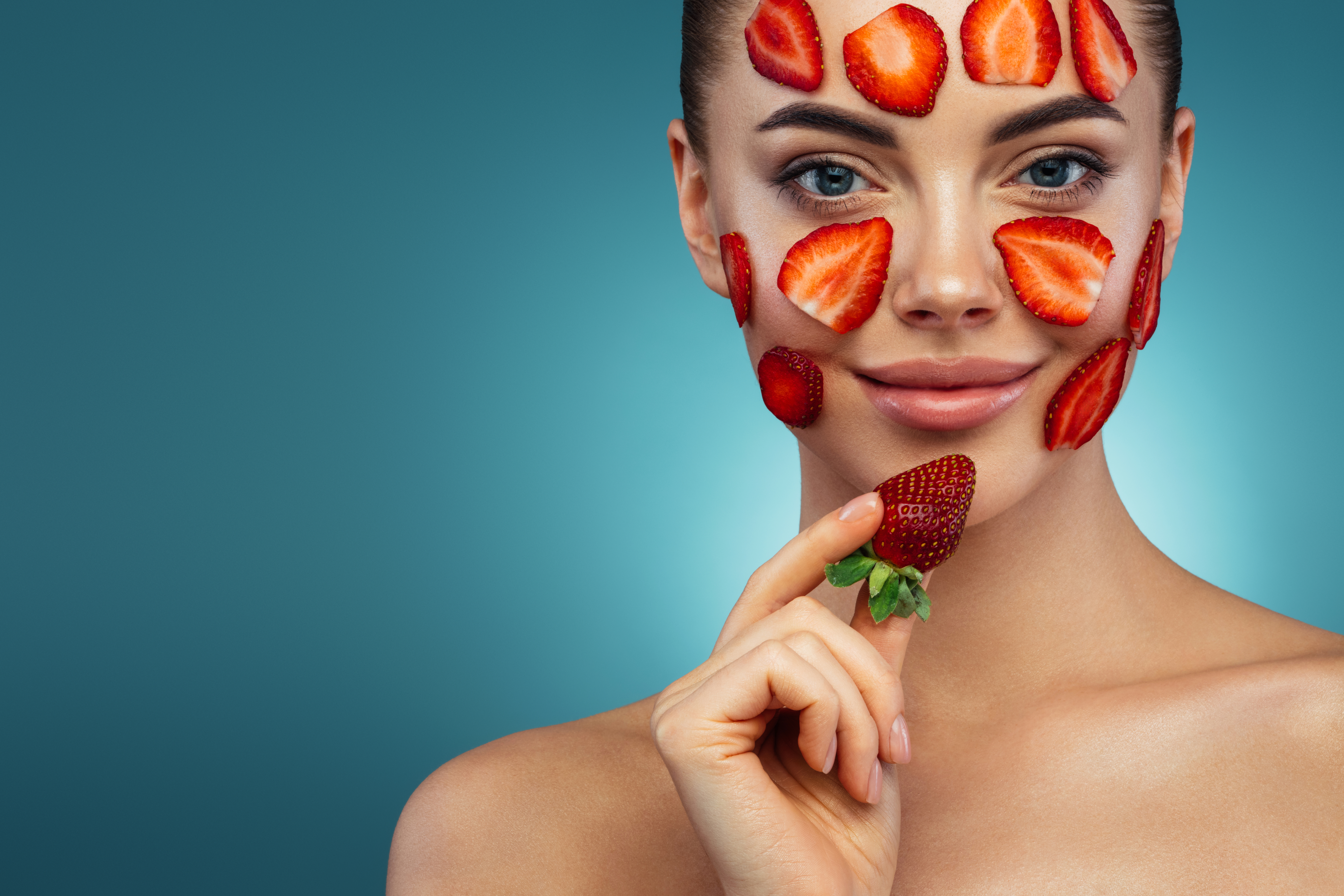 Happy young girl with facial mask of strawberry on her face