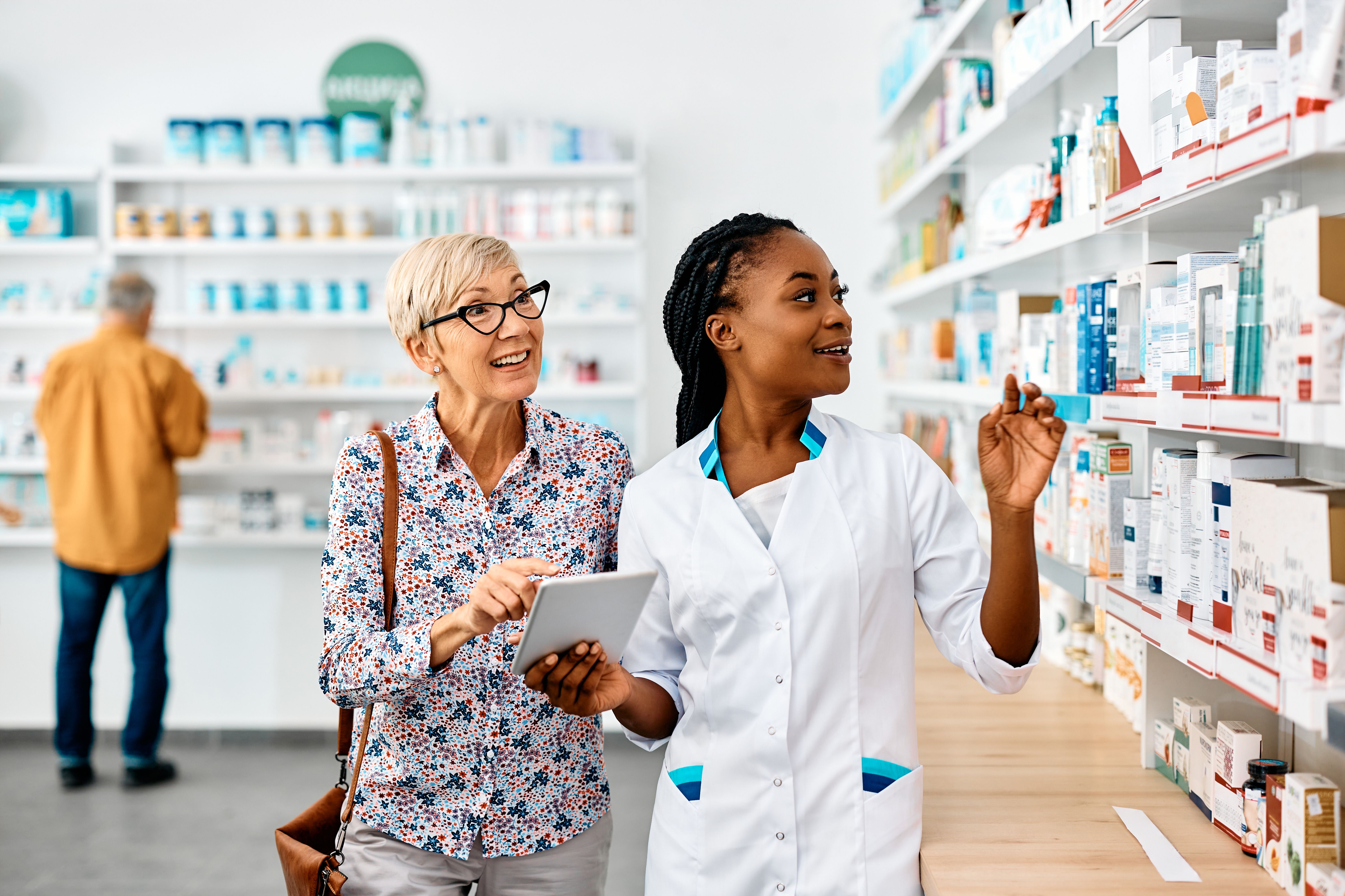 Young black pharmacist assisting senior woman in buying medicine in a pharmacy.