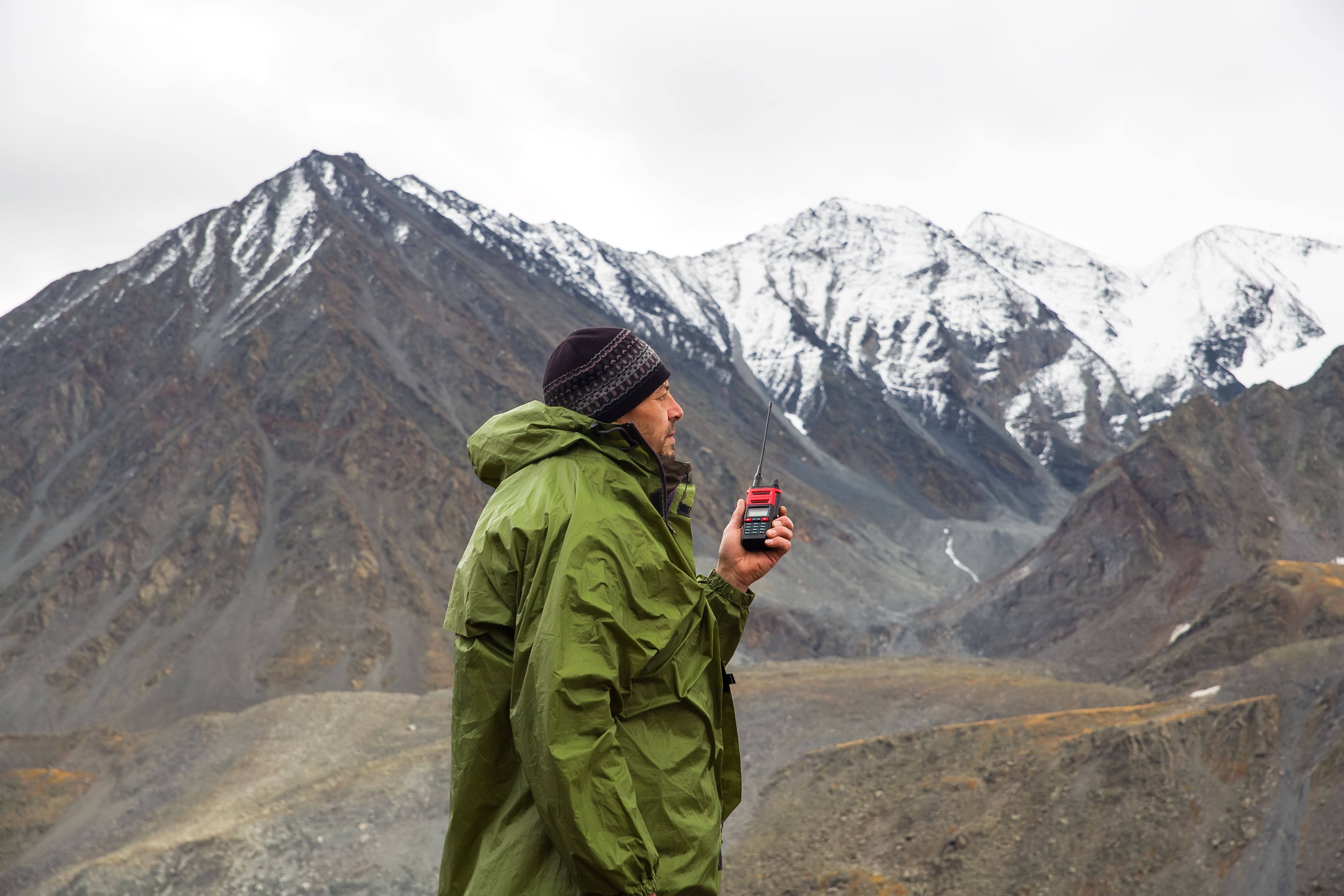 A man in the mountains talks on a walkie-talkie