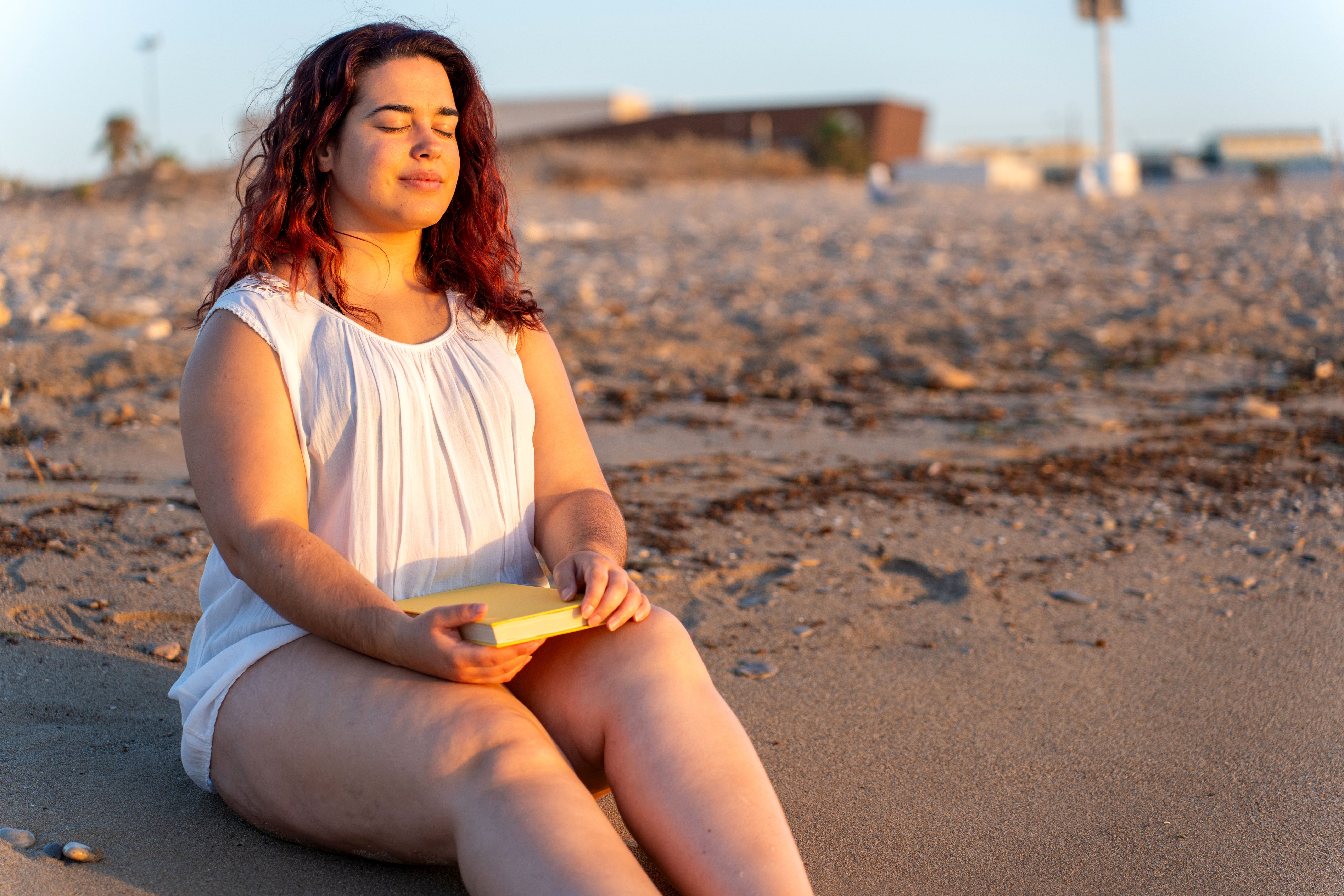 Curvy woman breathing and relaxing on the beach at sunset
