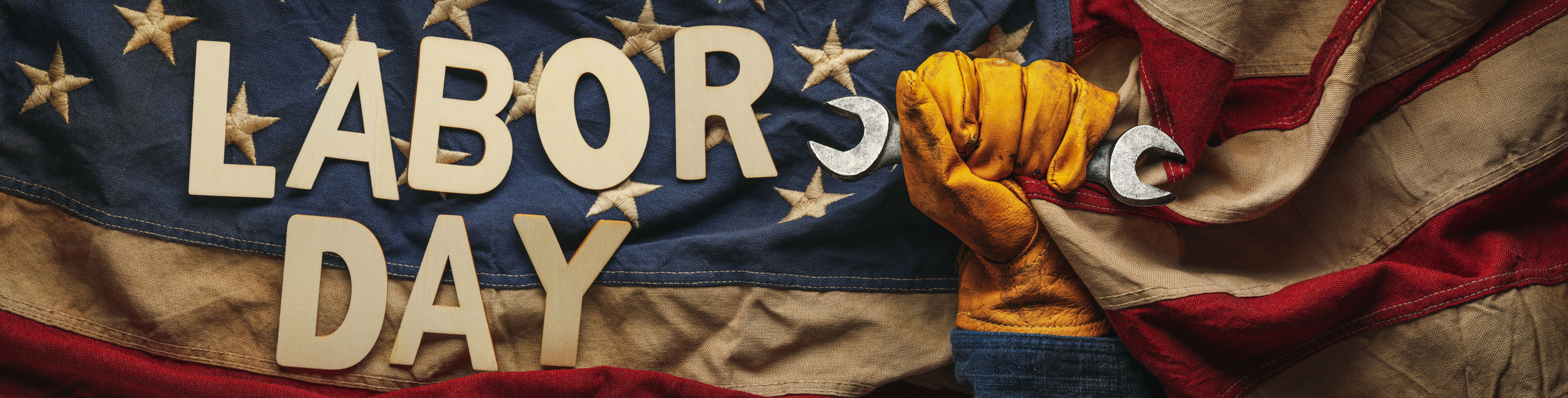 Old US American flag held by a worn work glove holding a crescent wrench with Labor day text. Labor day and American blue collar worker concept.