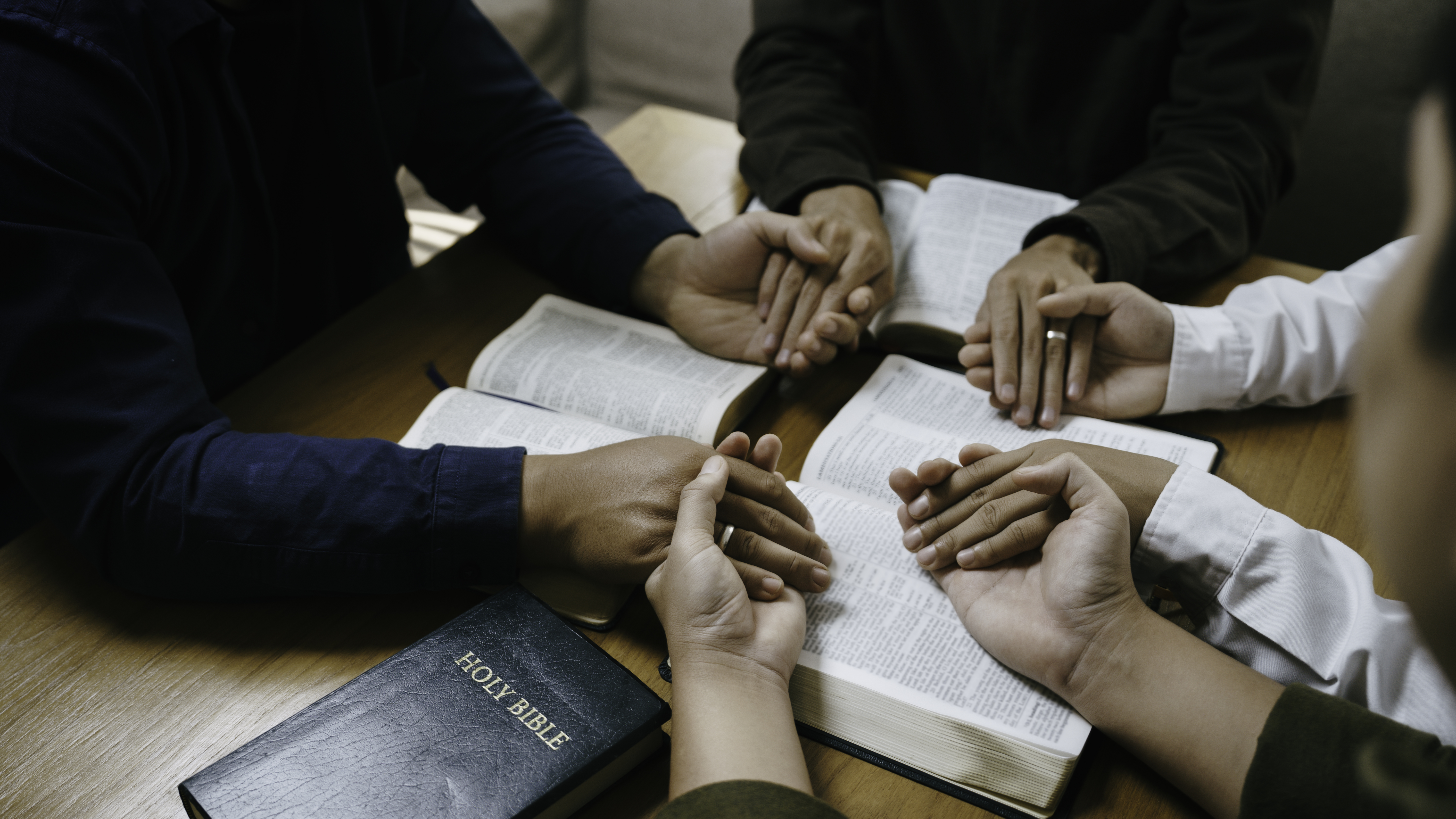 Christian Family prayer and worship. Christian group of people holding hands and praying worships to believe and Bible on a wooden table prayer meeting concept. Church Community pray together