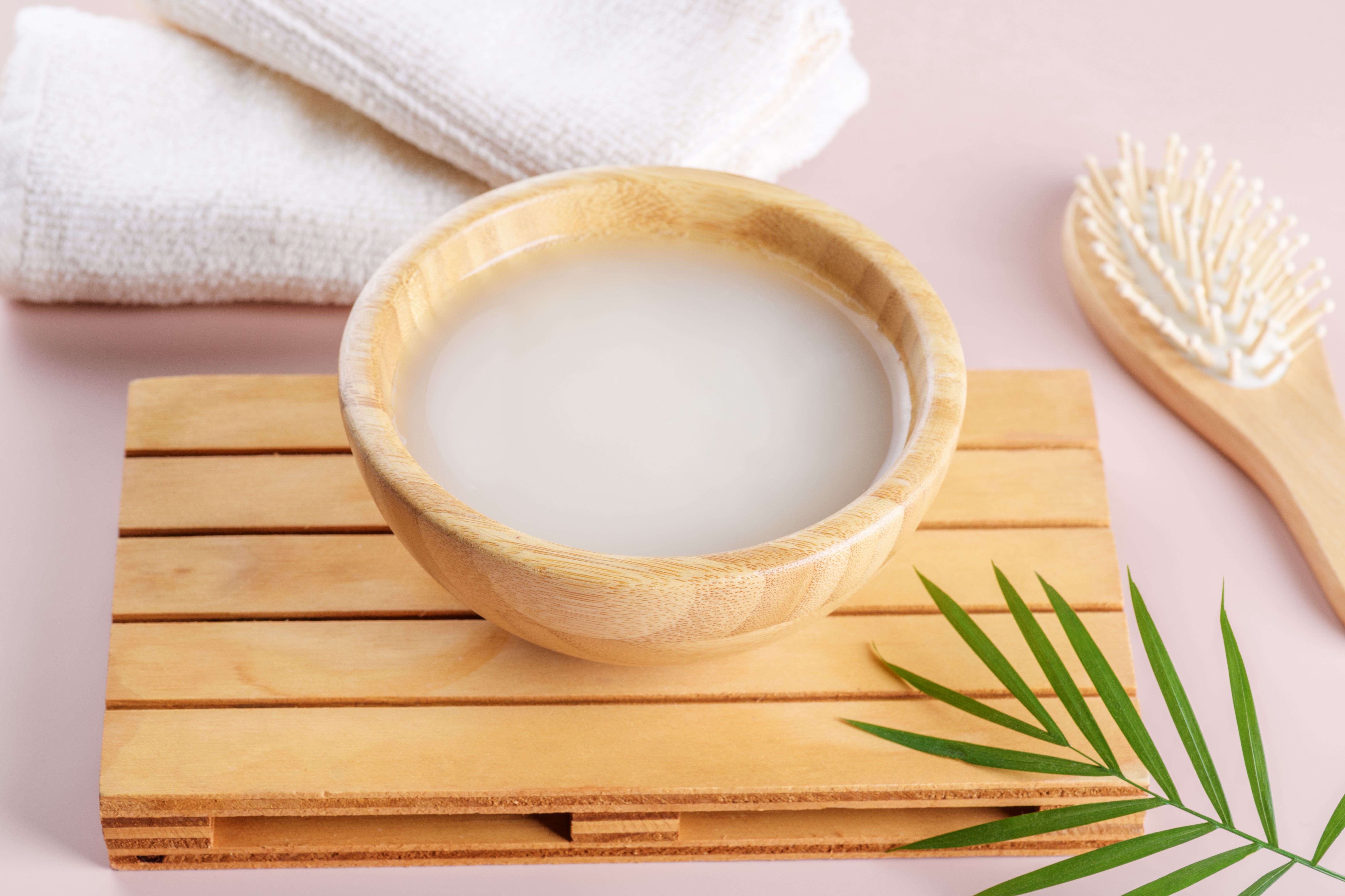 Homemade cosmetic rice water on wooden podium and towel on beige pastel background