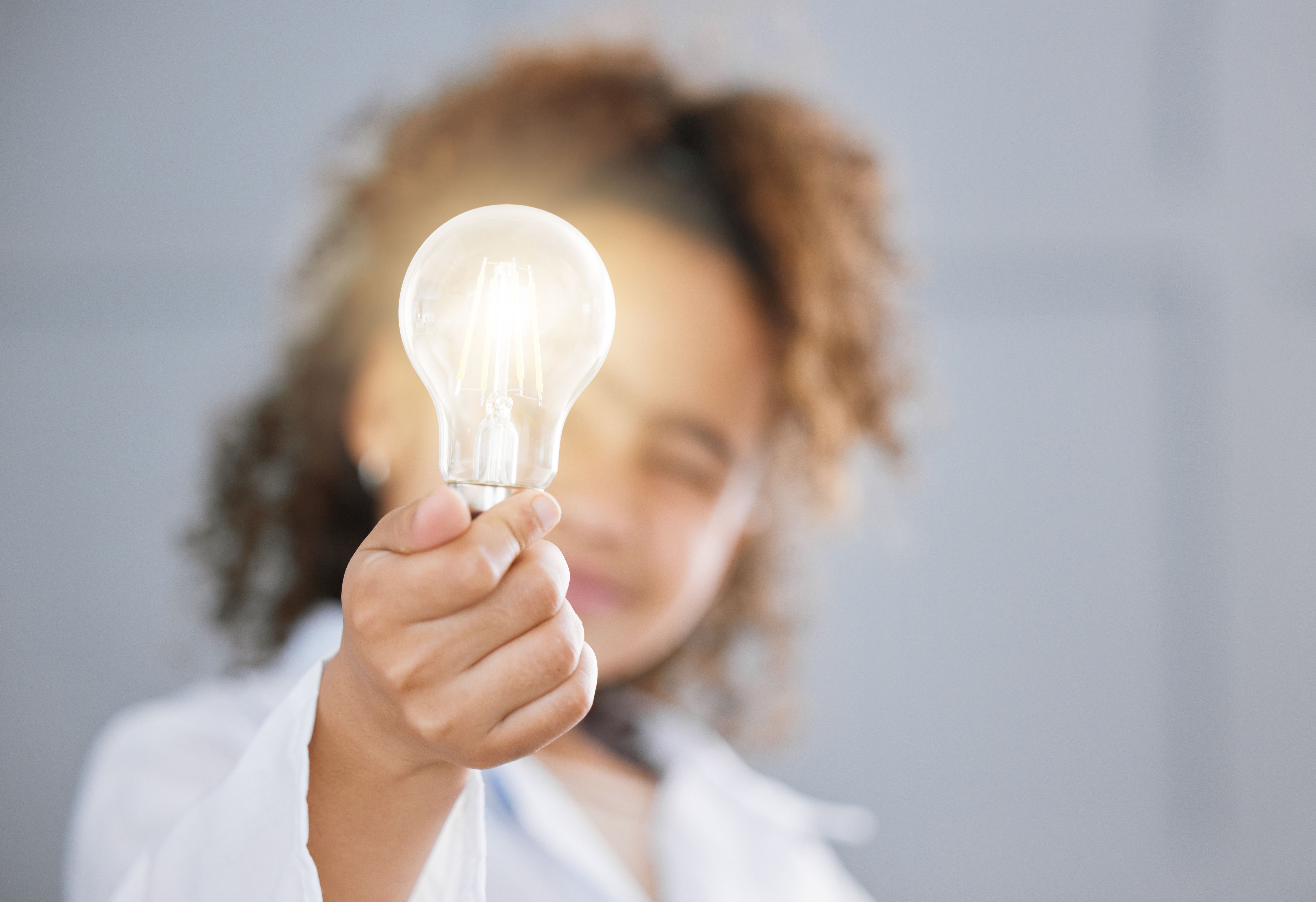 Cropped shot of an adorable little girl wearing a labcoat and holding out a lightbulb toward the camera Cropped shot of an adorable little girl wearing a labcoat and holding out a lightbulb toward the camera