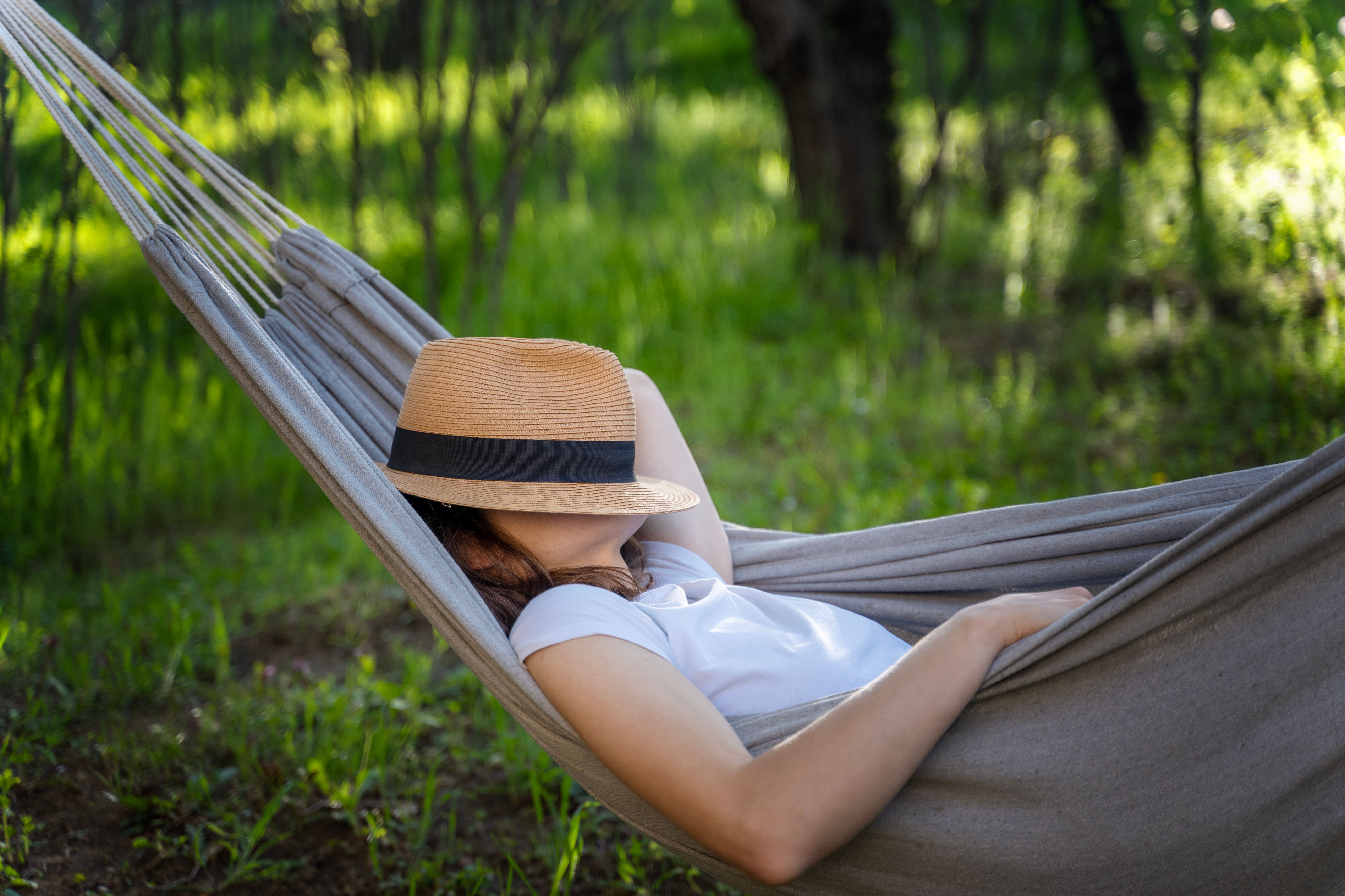 Femme se reposant dans un hamac dans un jardin d’été couvrant son visage avec un chapeau de paille. Vacances d’été