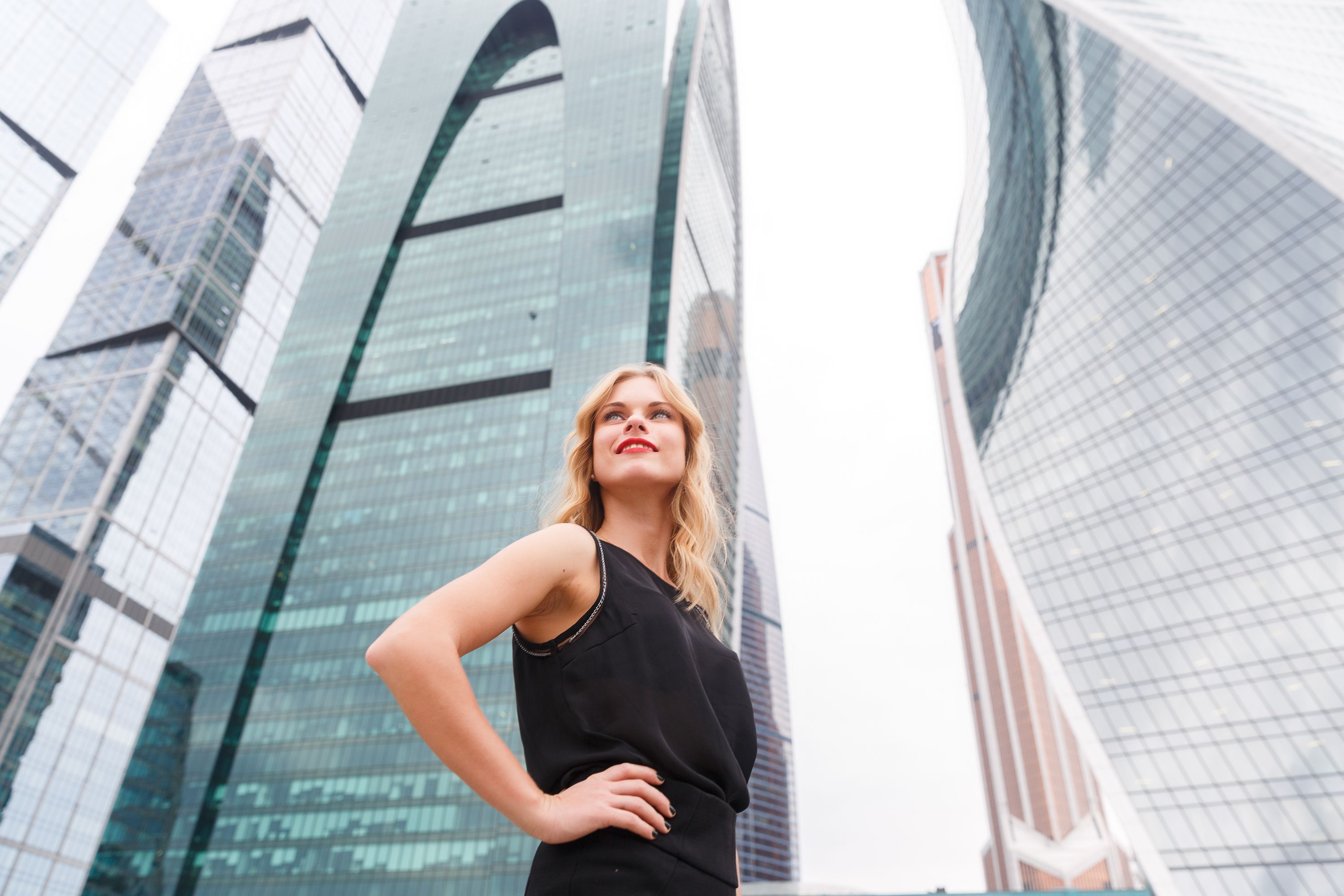 Confident blonde woman with arms akimbo on skyscraper background Confident blonde woman with arms akimbo on skyscraper background