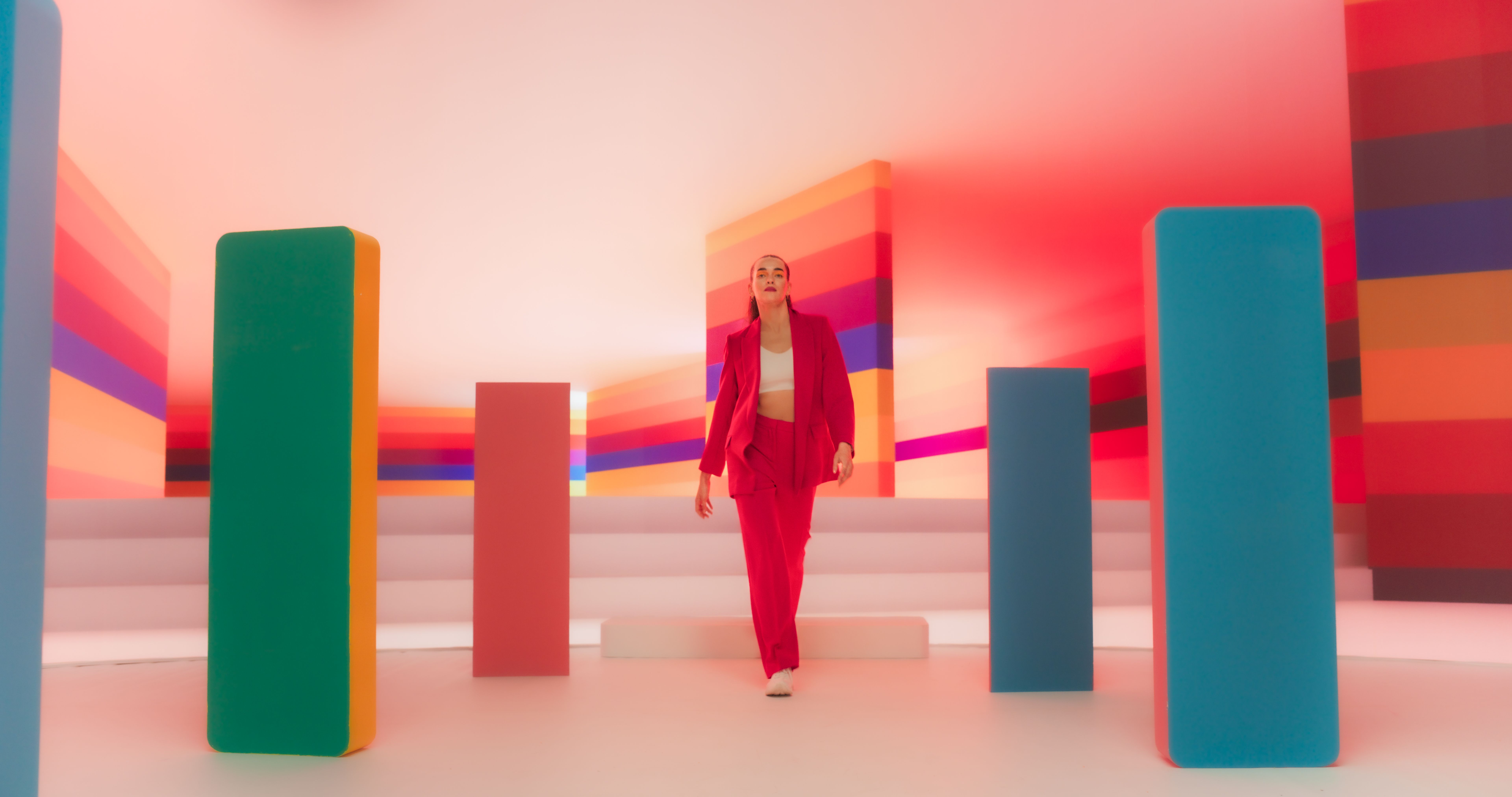 Low Angle Portrait of a Fashionable Young Caucasian Woman Performing a Catwalk in a Colorful Neon Studio. Stylish Female Walking Confidently In A Bright Lit Room With Geometric Decoration On Set