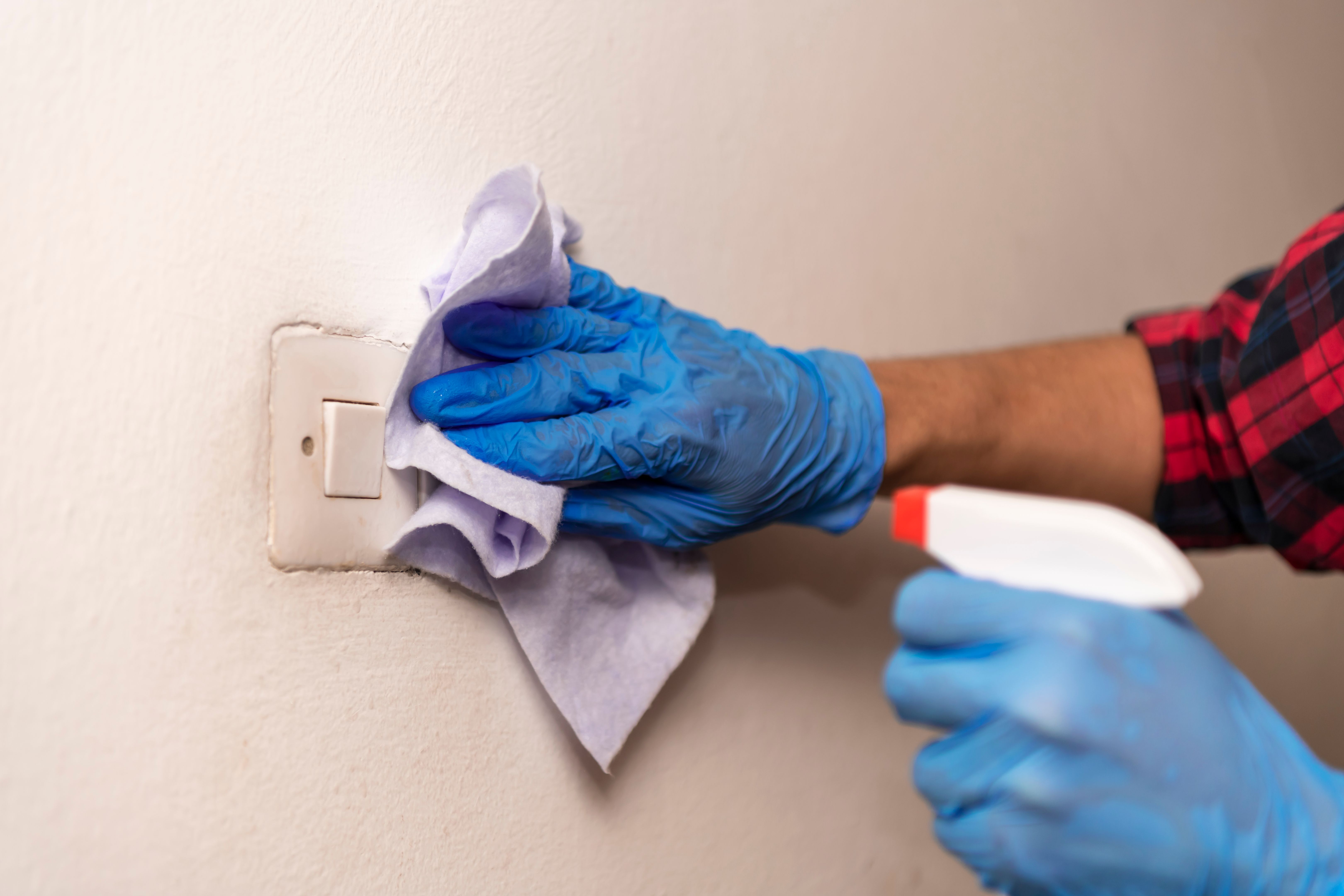A Man with Protective Gloves is Using an Alcohol Spray Bottle and a Rag to Clean the House.