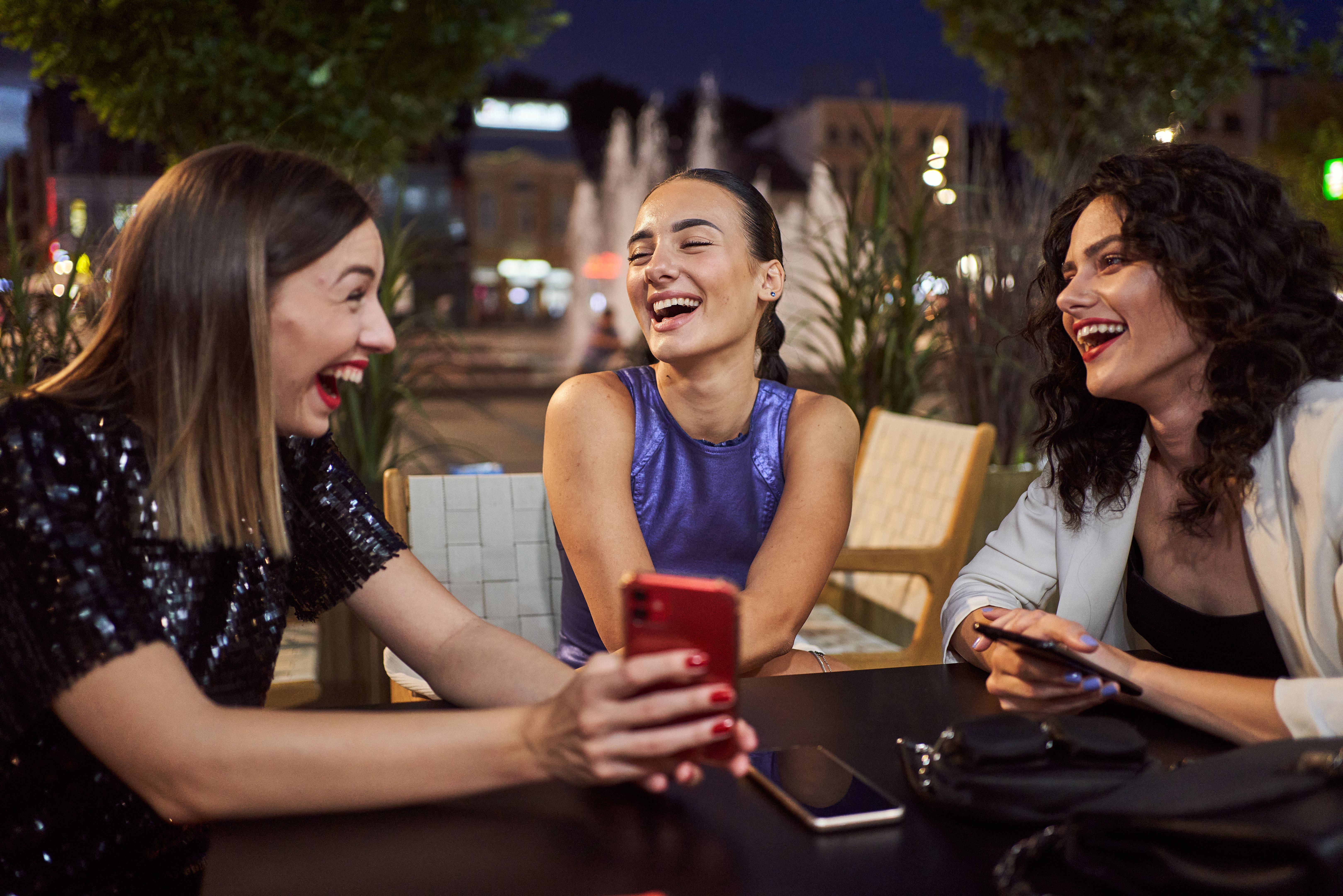 Ecstatic women laughing while looking at a mobile phone at a cafe