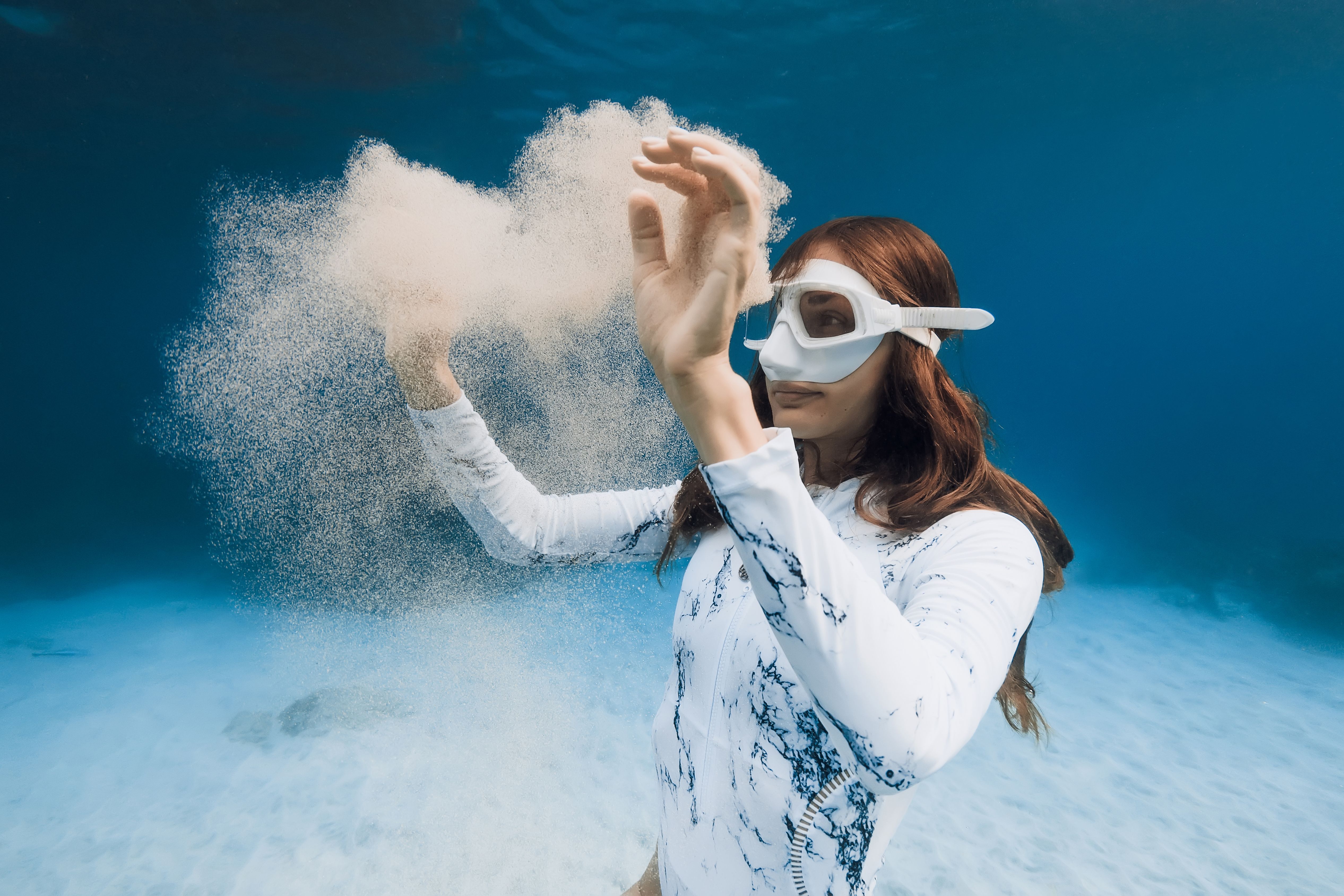 Gorgeous woman free diver posing with cloud of sand underwater in blue ocean. Close up portrait of freediver girl