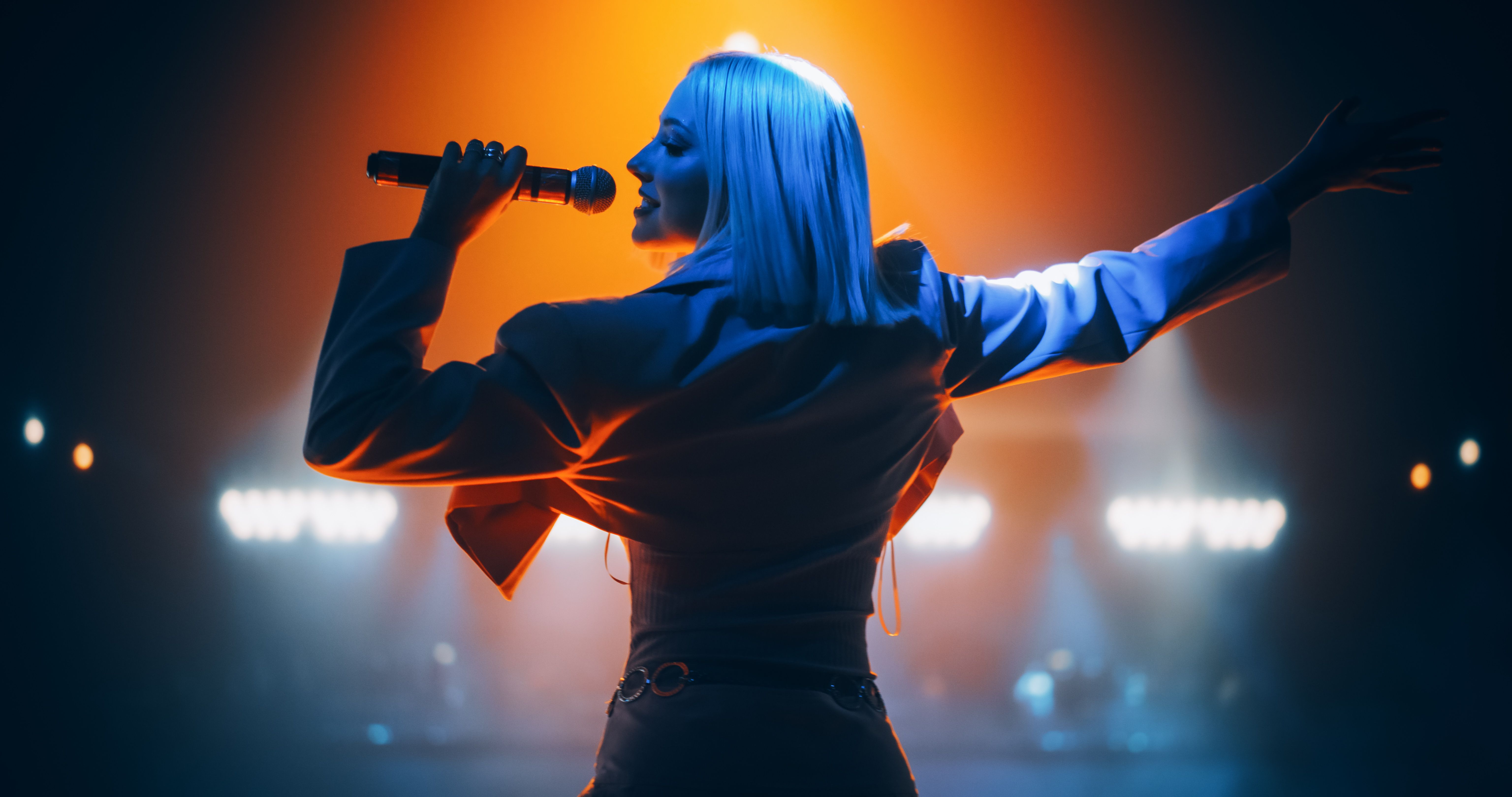 Energetic Pop Artist Performing on Stage in Pink Feminine Clothes. Excited Audience Listening to the Tunes and Being Illuminated by a Vibrant Light Show. Footage from the Back