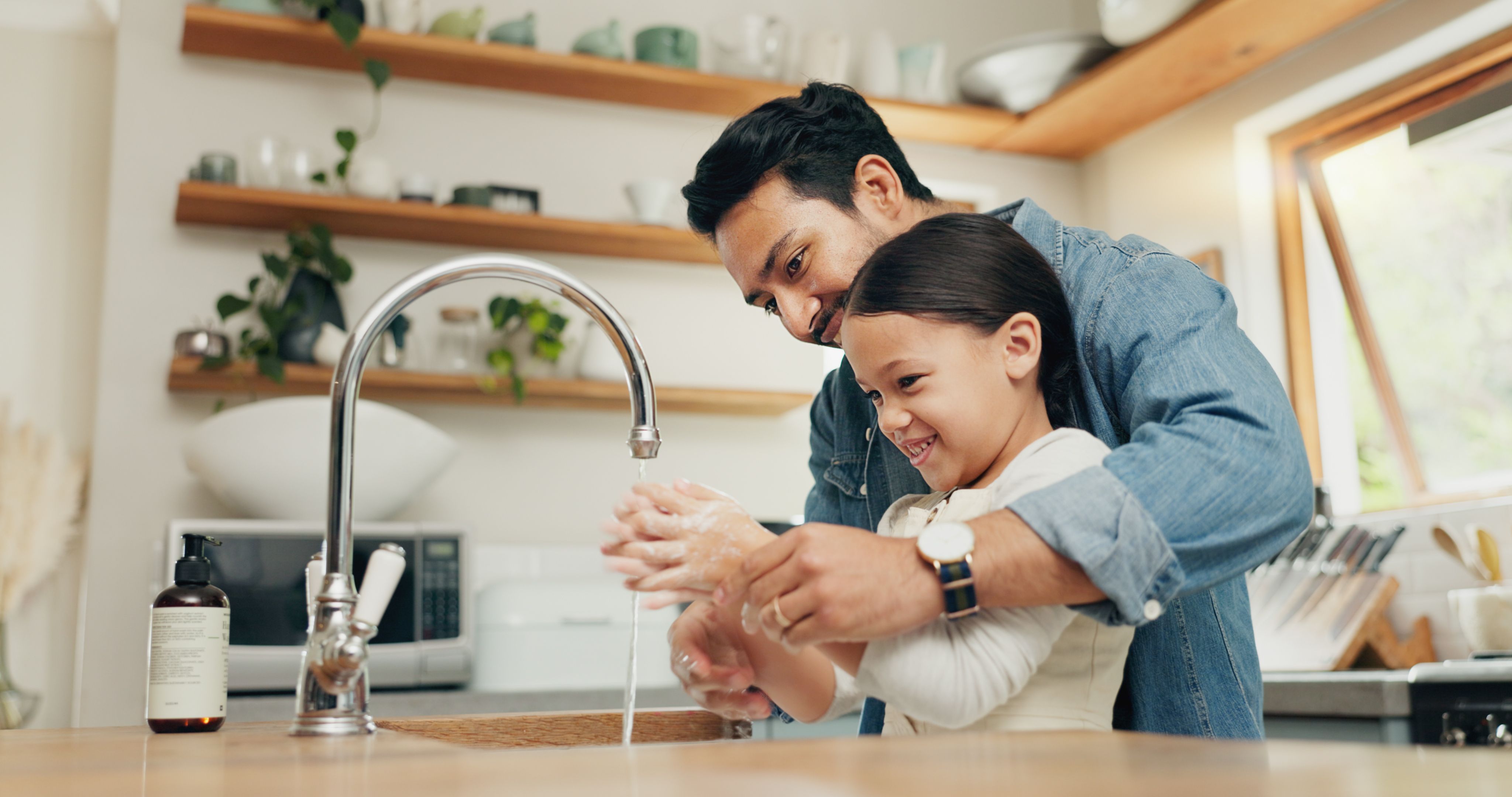 Girl washing her hands with her father in the kitchen for hygiene, health and wellness at home. Child learning to clean her skin with young dad with soap and water to prevent germs, dirt or bacteria. Girl washing her hands with her father in the kitchen for hygiene, health and wellness at home. Child learning to clean her skin with young dad with soap and water to prevent germs, dirt or bacteria.