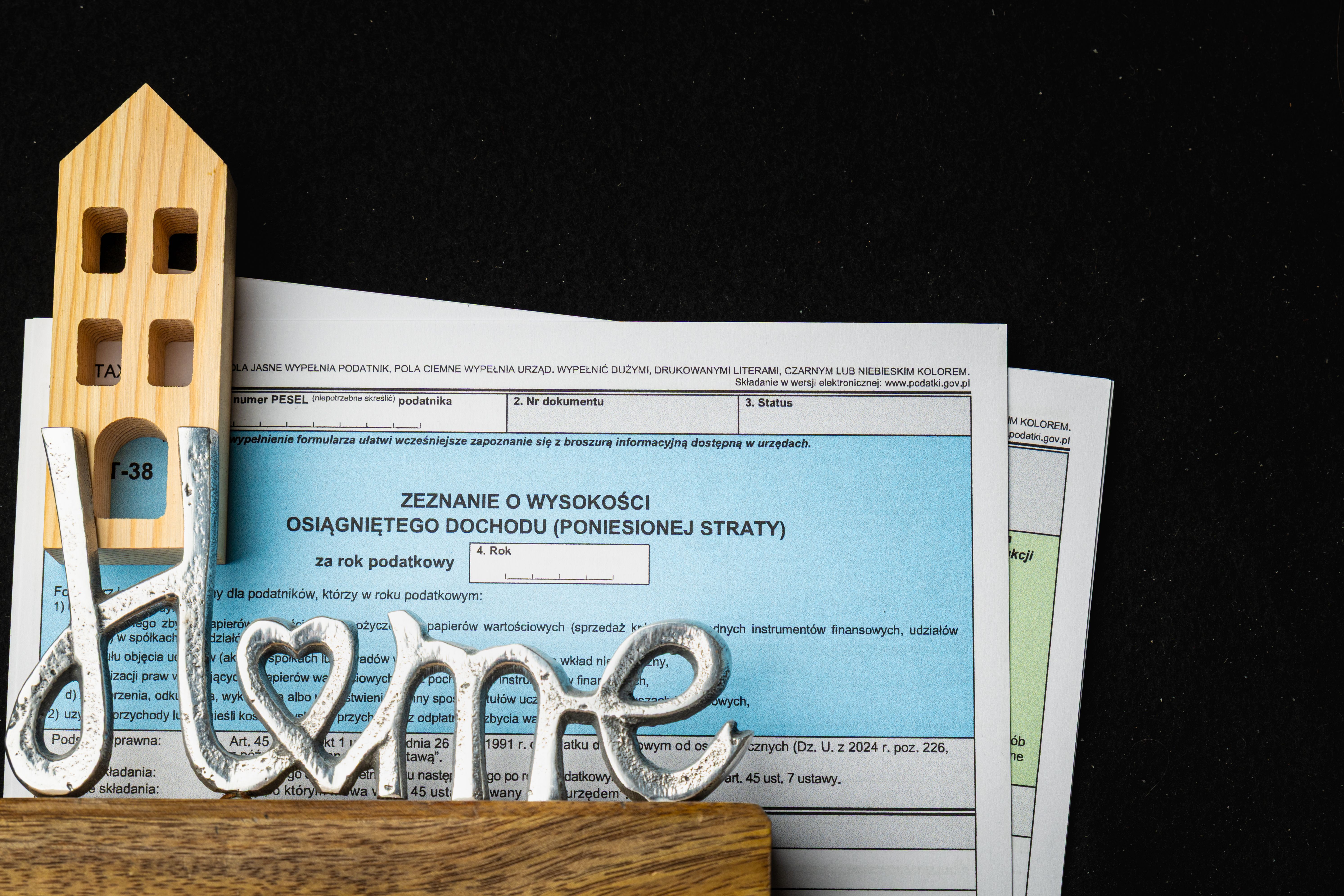 Polish PIT tax forms with symbolic wooden house and decorative metal word on table
