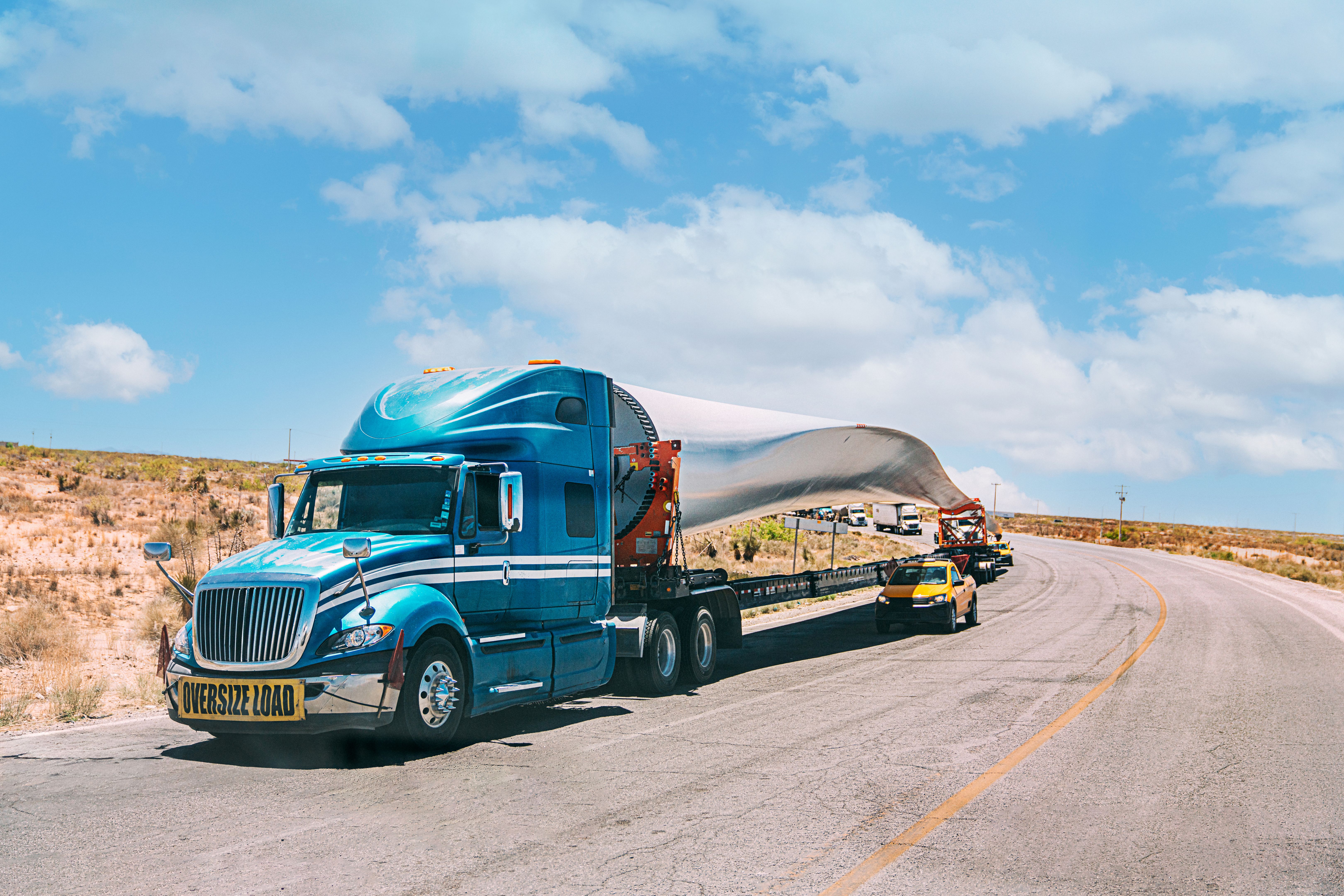 Diesel Semi Truck pulling a Trailer with a Green Energy Wind Turbine Propeller, Delivering as Imported Goods from Mexico into the United States across the Border