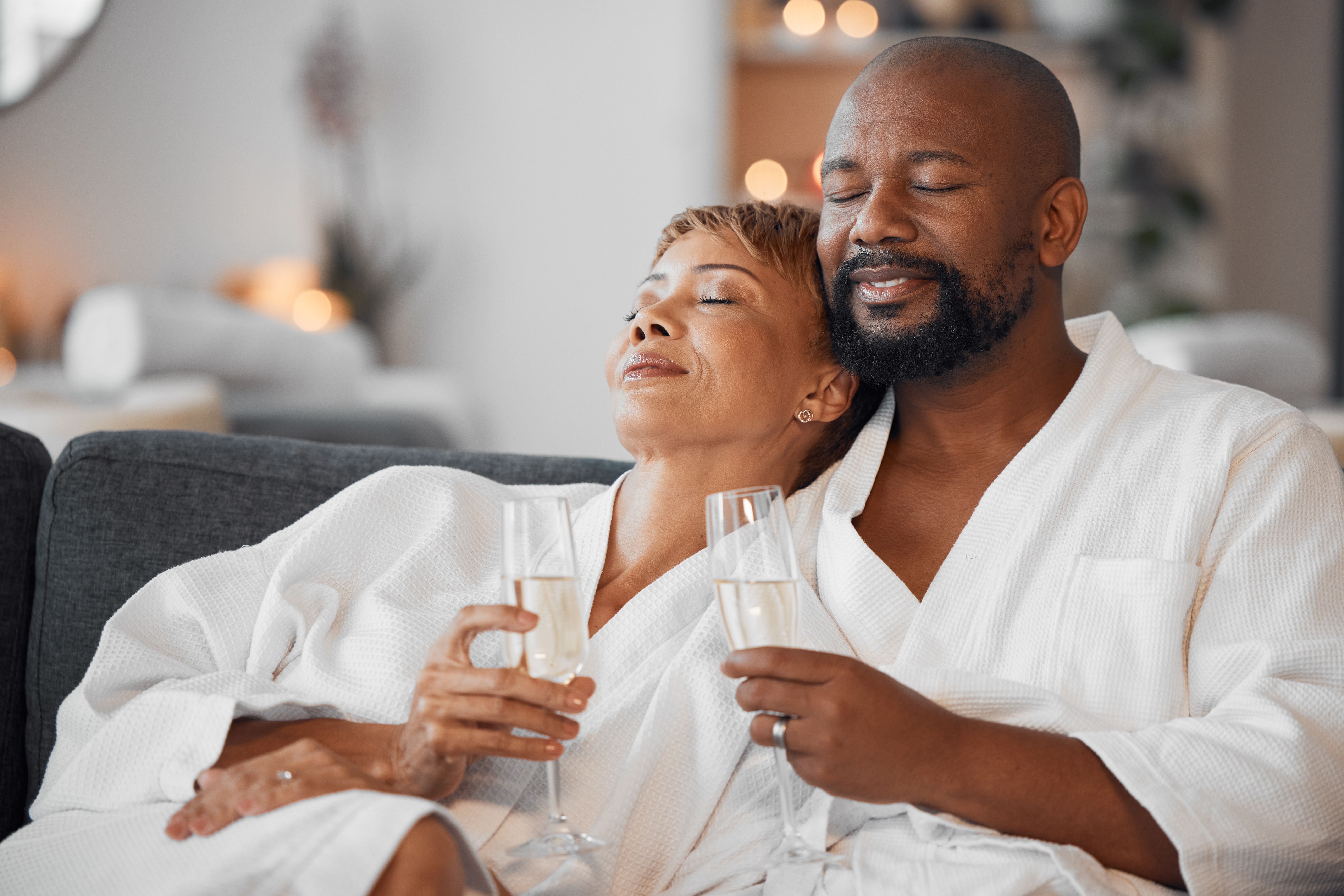 Spa couple, champagne and relax in wellness salon for love, hospitality and calm therapy at luxury hotel, vacation or peace together. African man, black woman and drinking wine after skincare massage
