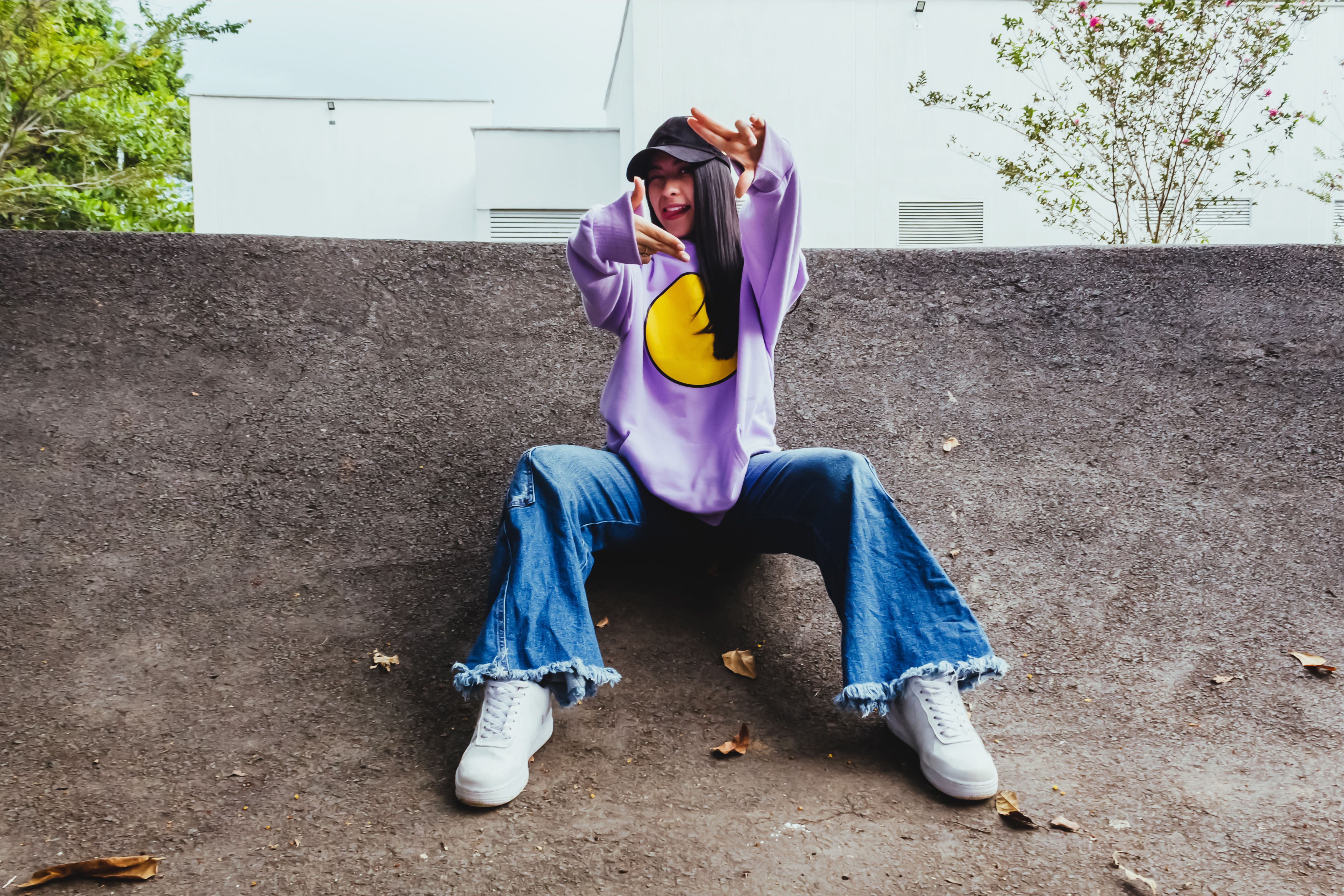 beautiful teenage girl in sweatshirt and cap sitting in the city in urban style