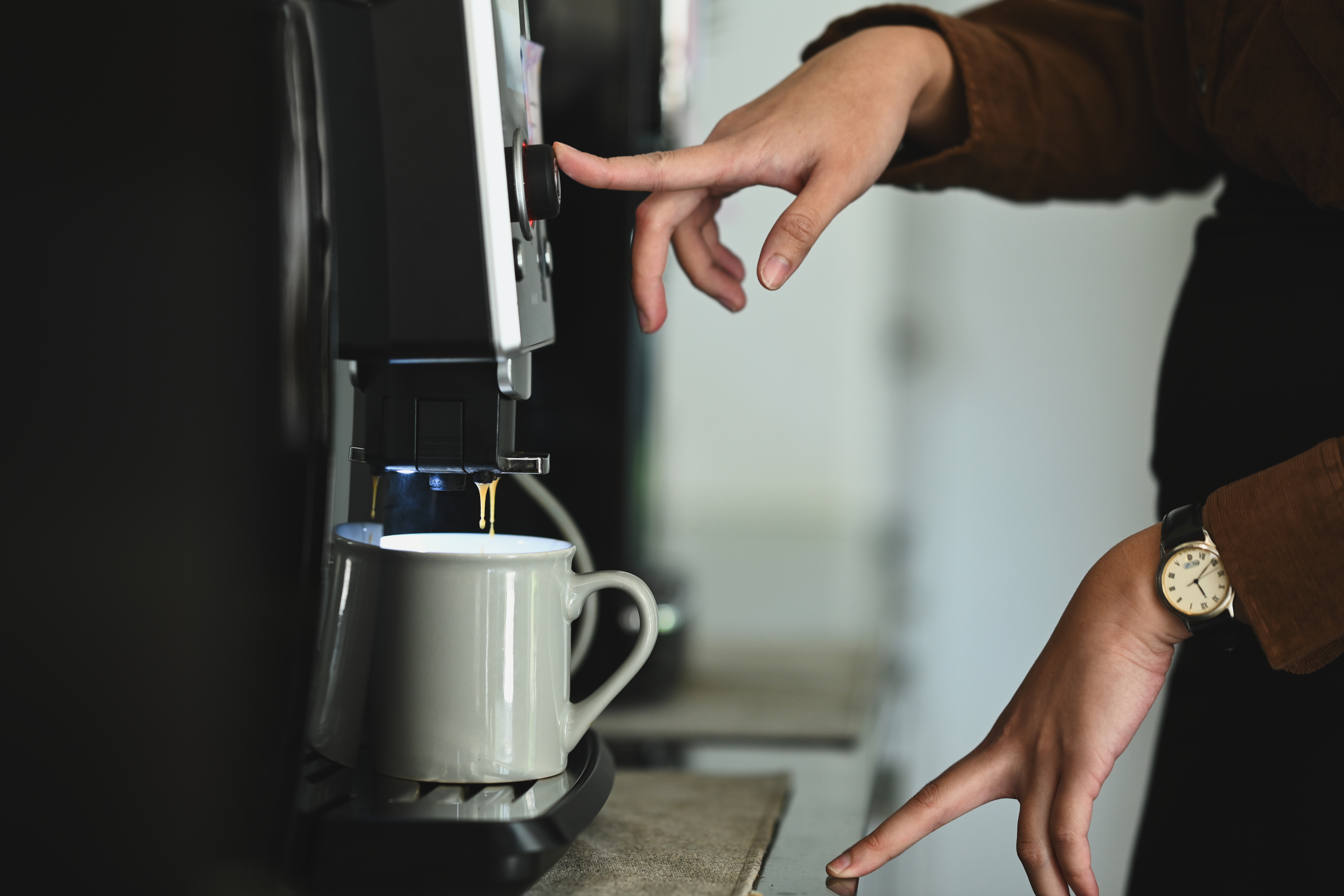 Side view of woman preparing fresh aromatic coffee, using a coffee machine maker in cozy office kitchen. Side view of woman preparing fresh aromatic coffee, using a coffee machine maker in cozy office kitchen.